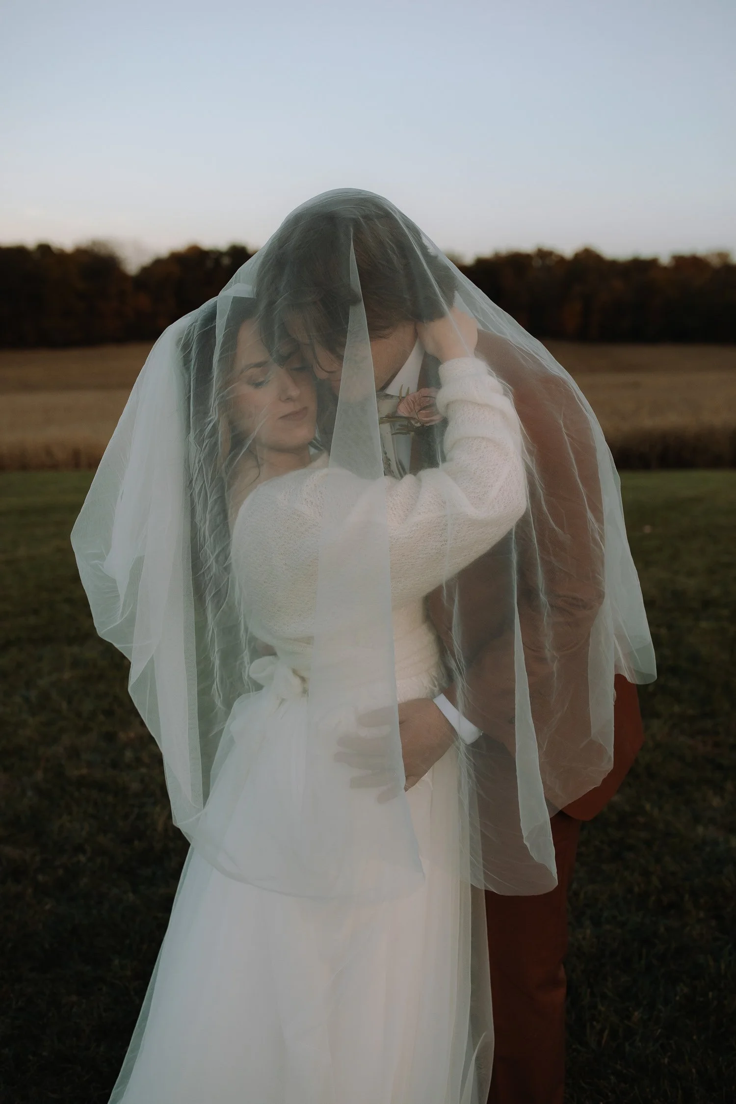 Bride and groom wrapped in a veil during dusk wedding portraits at Ivory Meadows in Dayton, Ohio, photographed with soft, natural light.