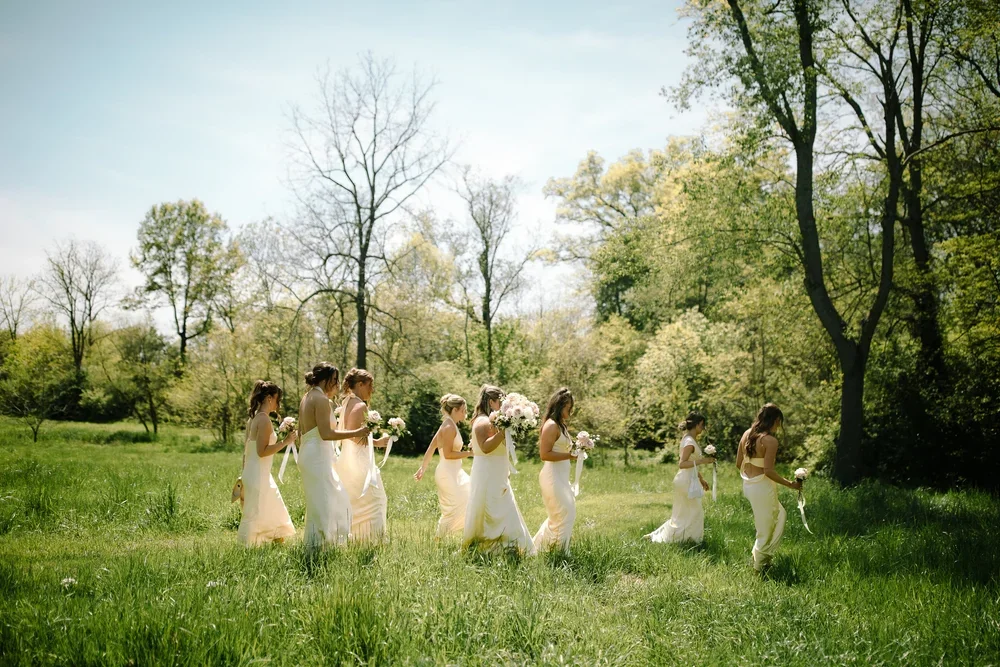 Bridesmaids walking through a sunlit field during a spring wedding at Jorgensen Farm The Gardens in Columbus, Ohio
