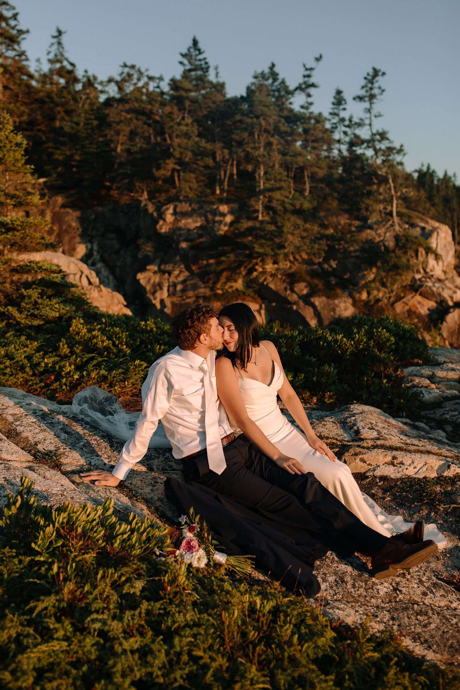 Intimate elopement portraits of a couple sitting together on the rocky Maine coastline during an Acadia National Park wedding day