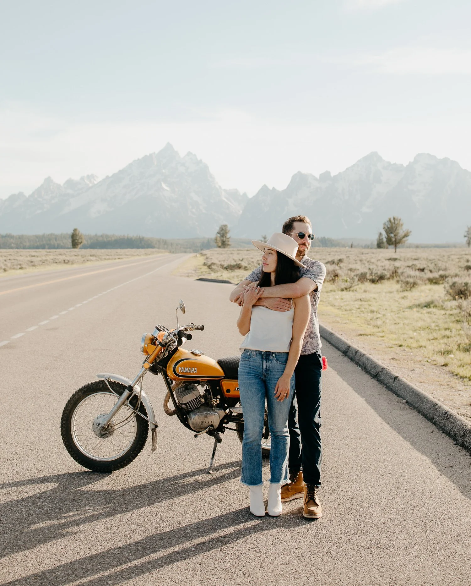 Couple standing beside a vintage motorcycle on an open road in Jackson Hole