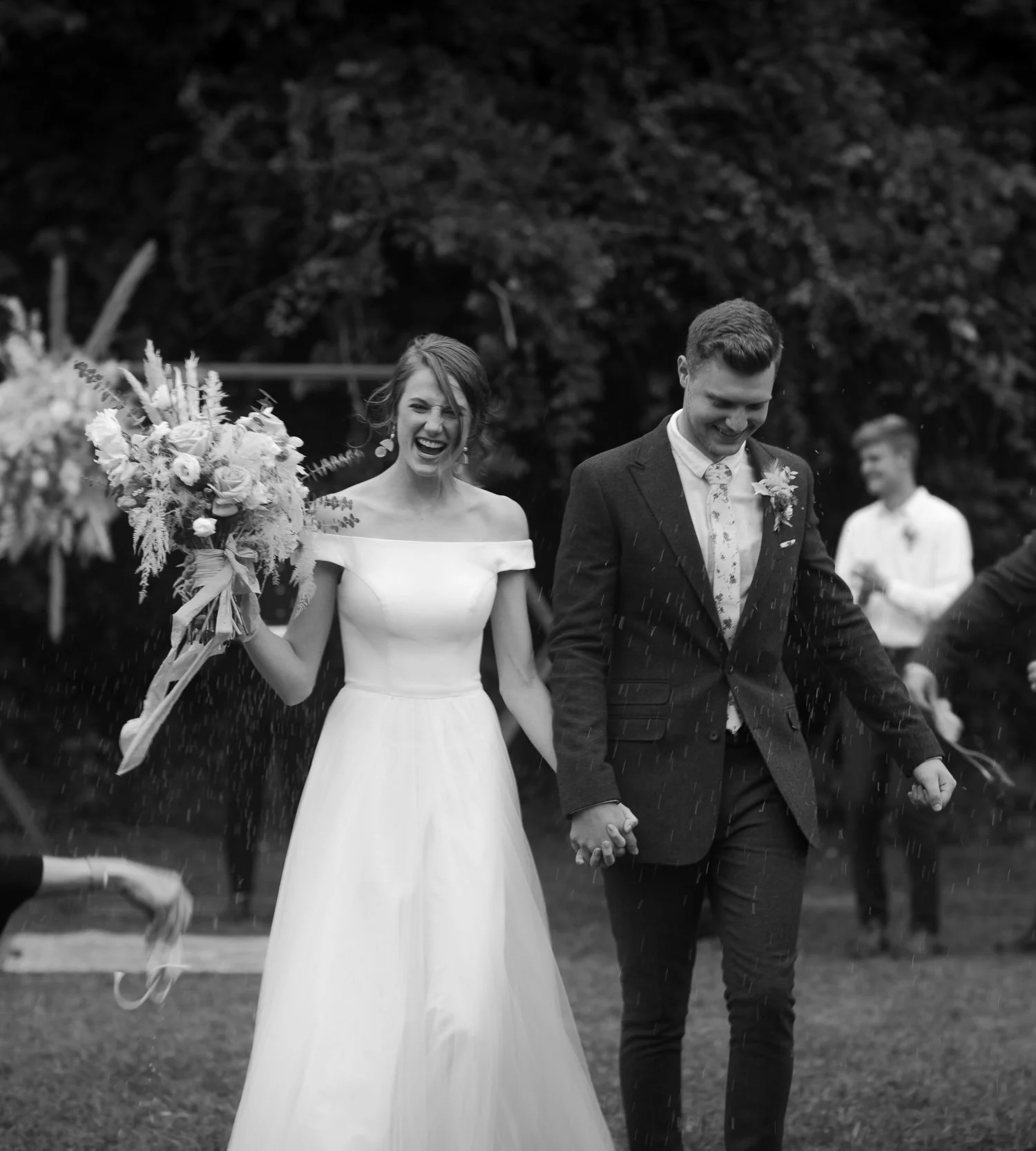 Bride and groom laughing while walking through rain during candid wedding exit captured in black and white