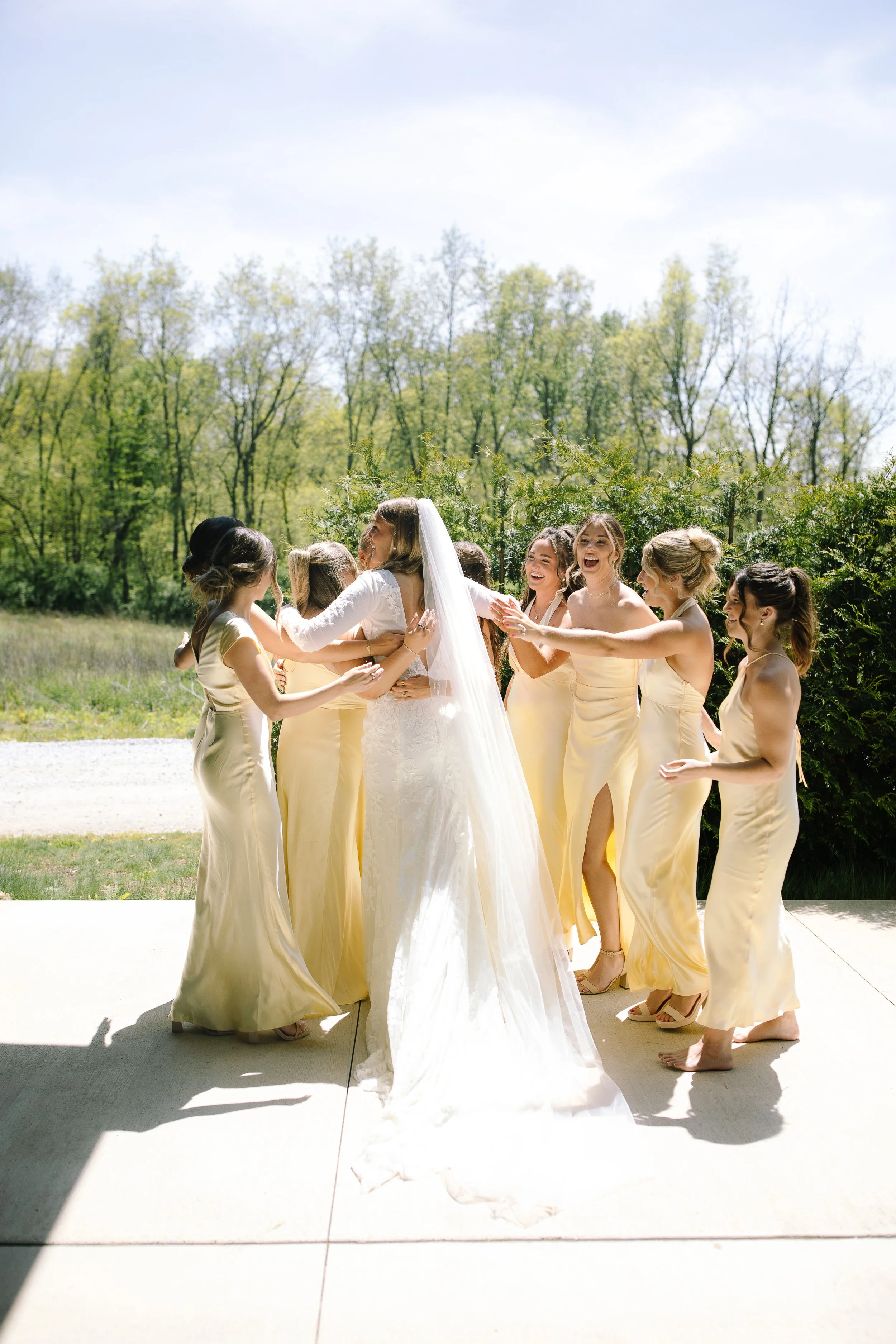 Bride hugging her bridesmaids in pale yellow dresses during a spring wedding at Jorgensen Farm The Gardens.