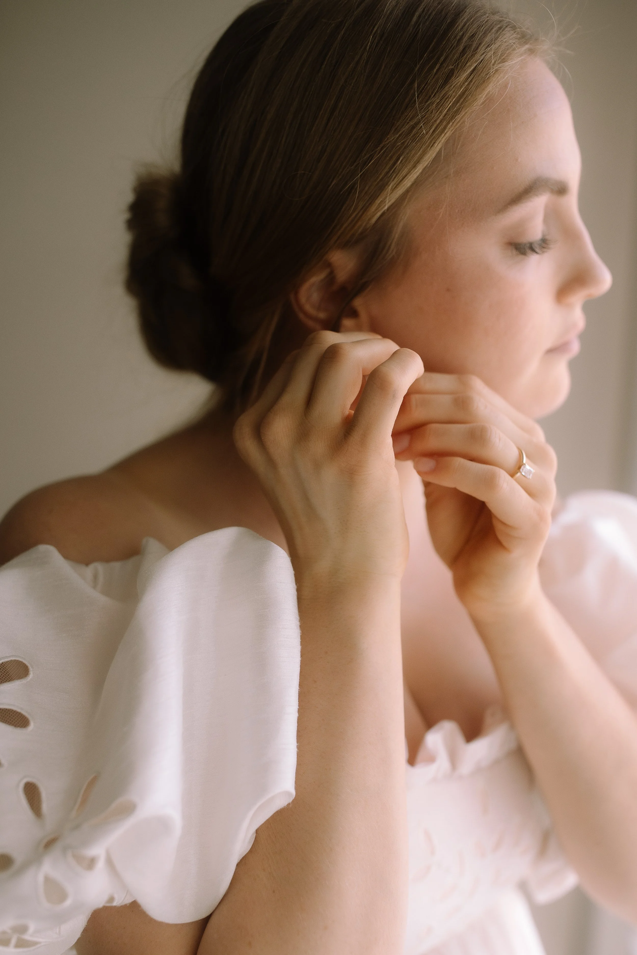 Close-up of bride putting on earrings in natural window light before her wedding ceremony.