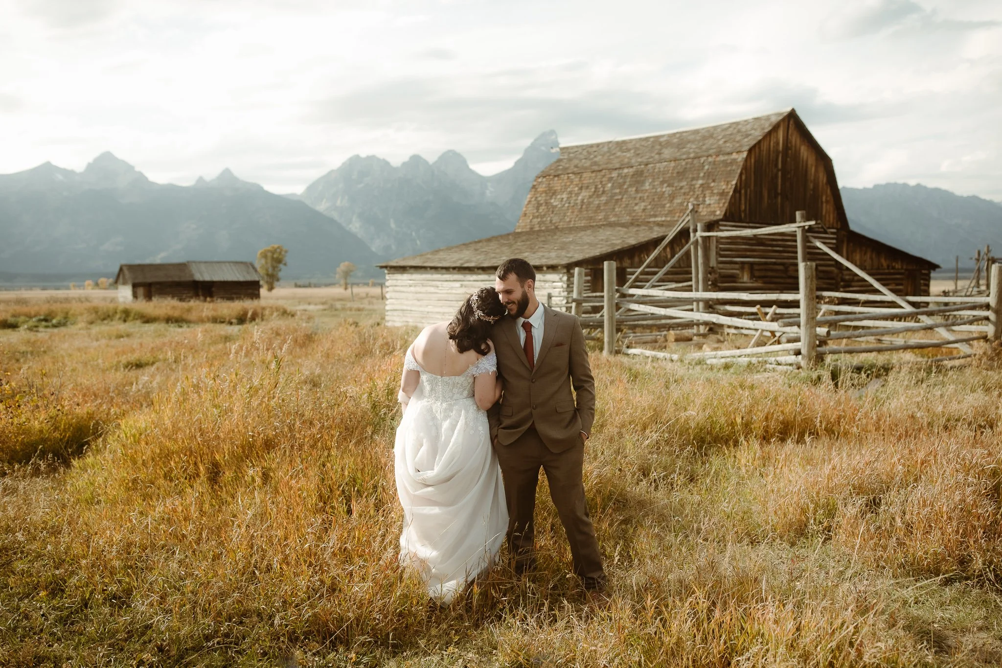 Bride and groom embracing near a historic barn at Mormon Row with the Teton range behind them