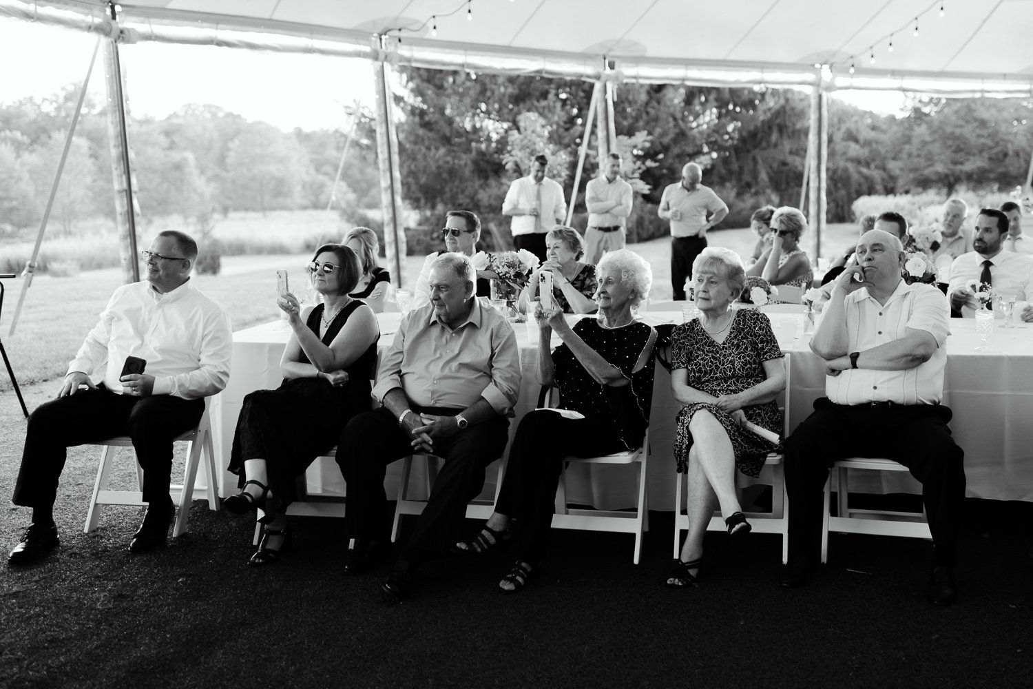 Wedding guests seated in a reception tent listening to speeches during the evening celebration