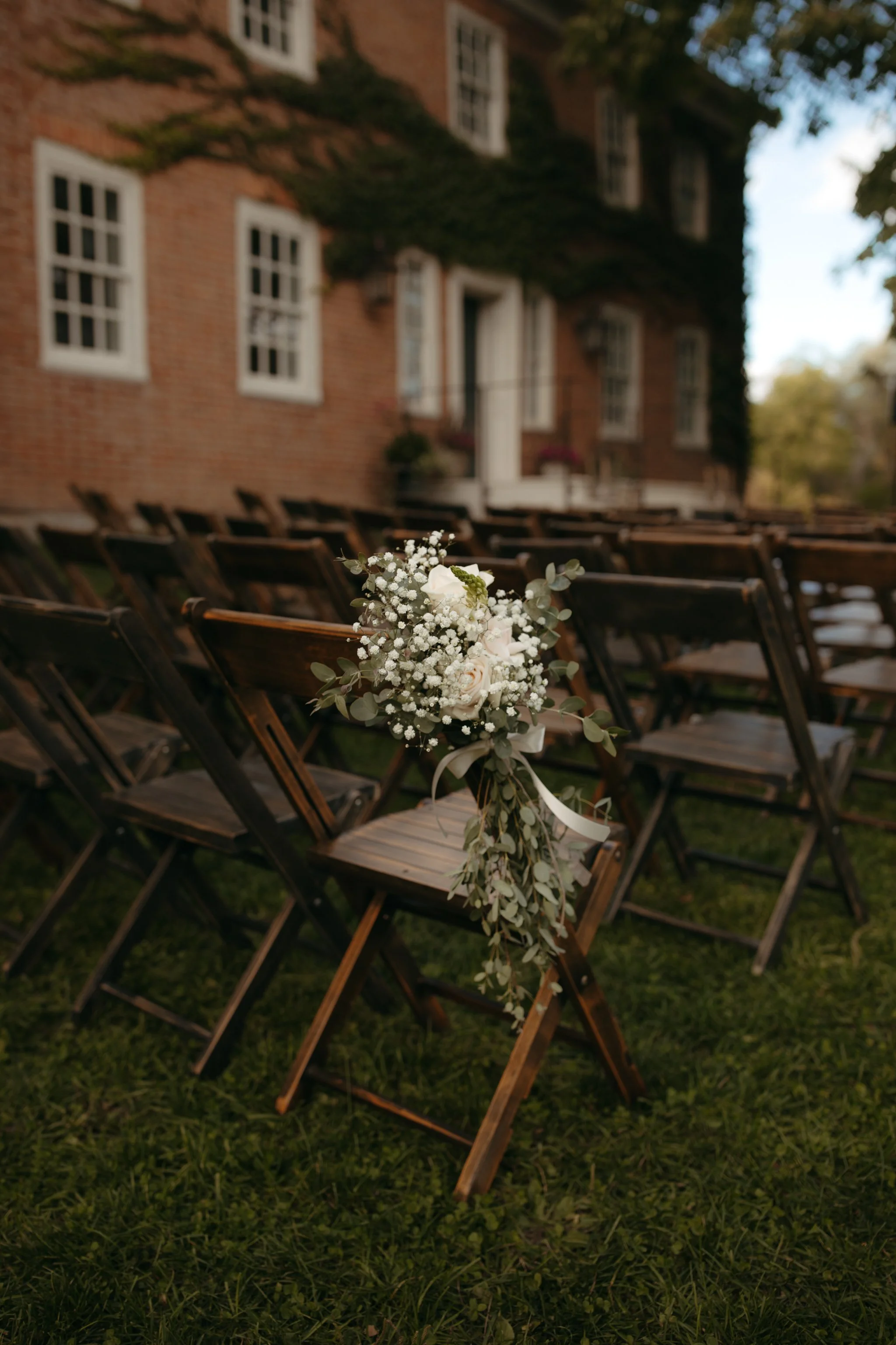 Floral arrangement tied to wooden ceremony chairs outside the historic brick estate at Windrift Hall in the Hudson Valley