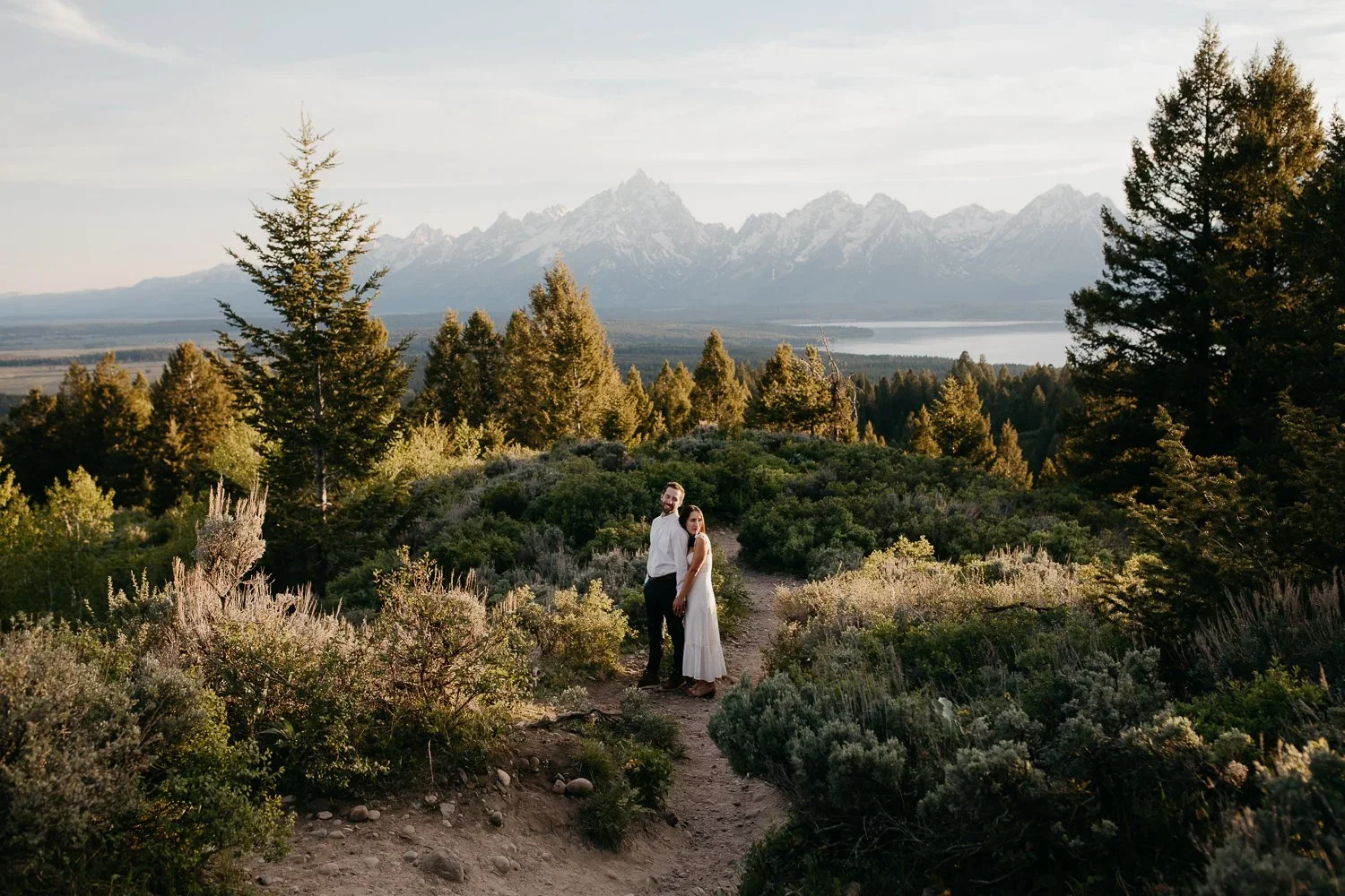Engaged couple standing on a trail with the Grand Teton range behind them in Jackson Hole, Wyoming