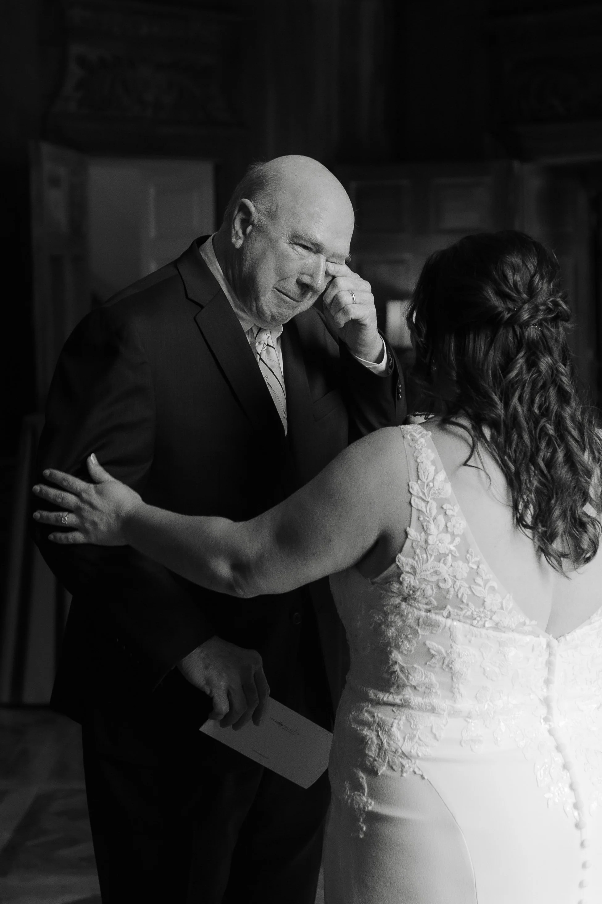 Close black and white photo of father and daughter sharing emotional hug during wedding