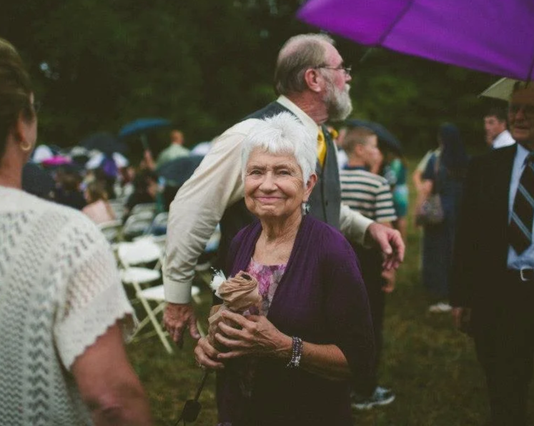 Candid wedding photo of grandmother holding umbrella during rainy ceremony, meaningful family wedding moment