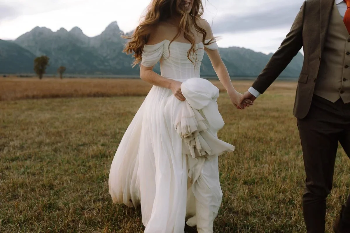 Bride and groom walking hand in hand through an open field with mountain views in Grand Teton National Park