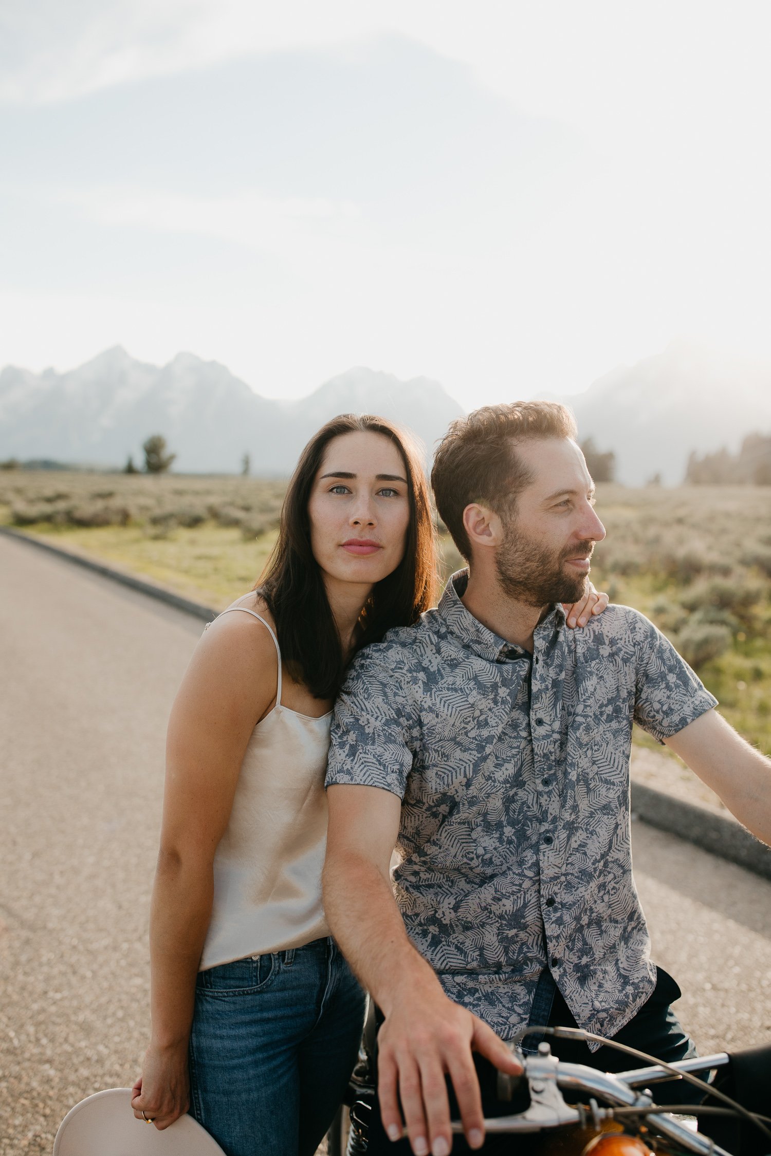 Engaged couple resting together beside a motorcycle on a quiet road