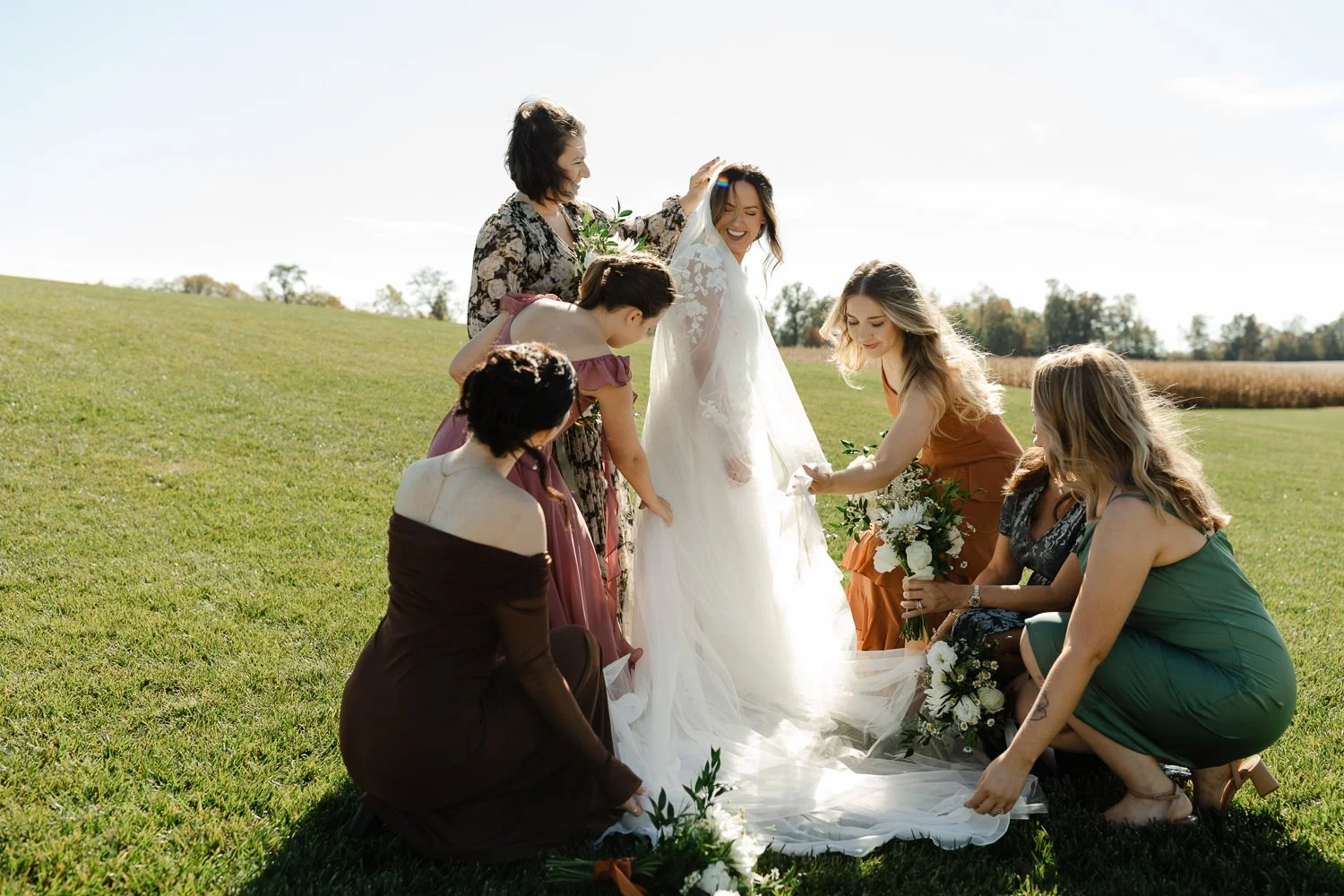 Bridesmaids helping adjust the bride’s veil and dress during outdoor portraits at Ivory Meadows in Yellow Springs, Ohio.