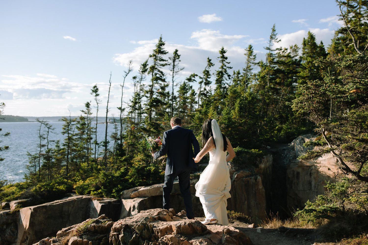 Bride and groom walking together toward a remote coastal overlook during an Acadia National Park elopement evening
