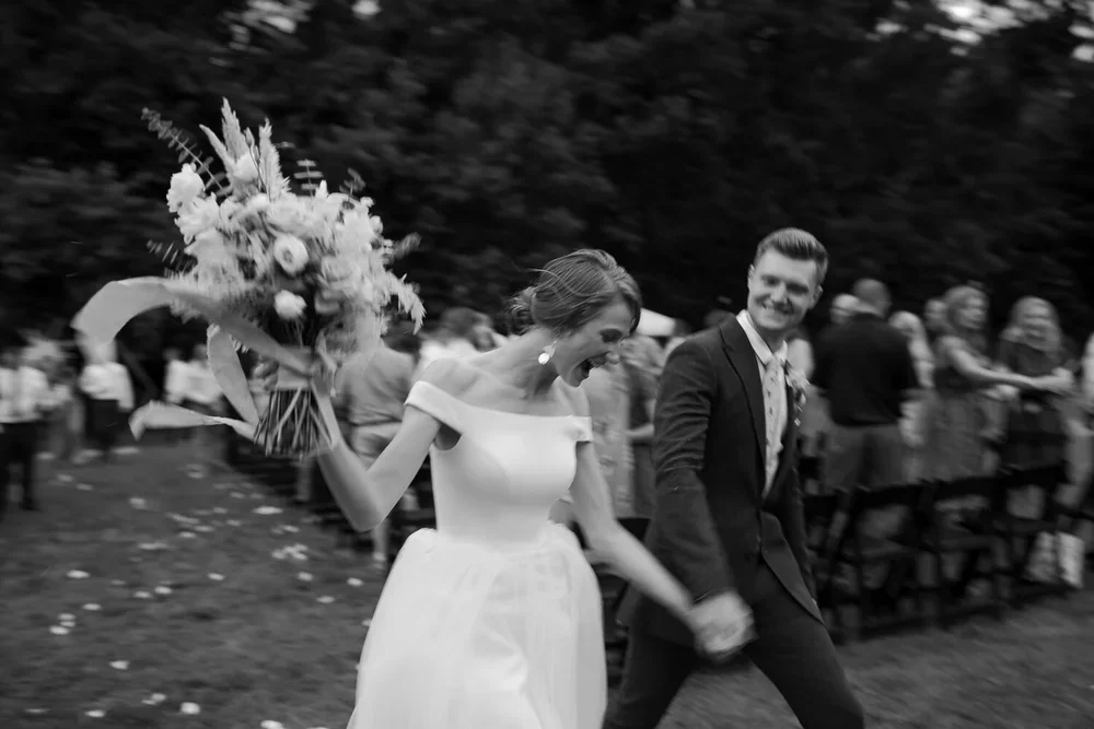 Bride and groom laughing while running hand in hand after ceremony captured in candid black and white
