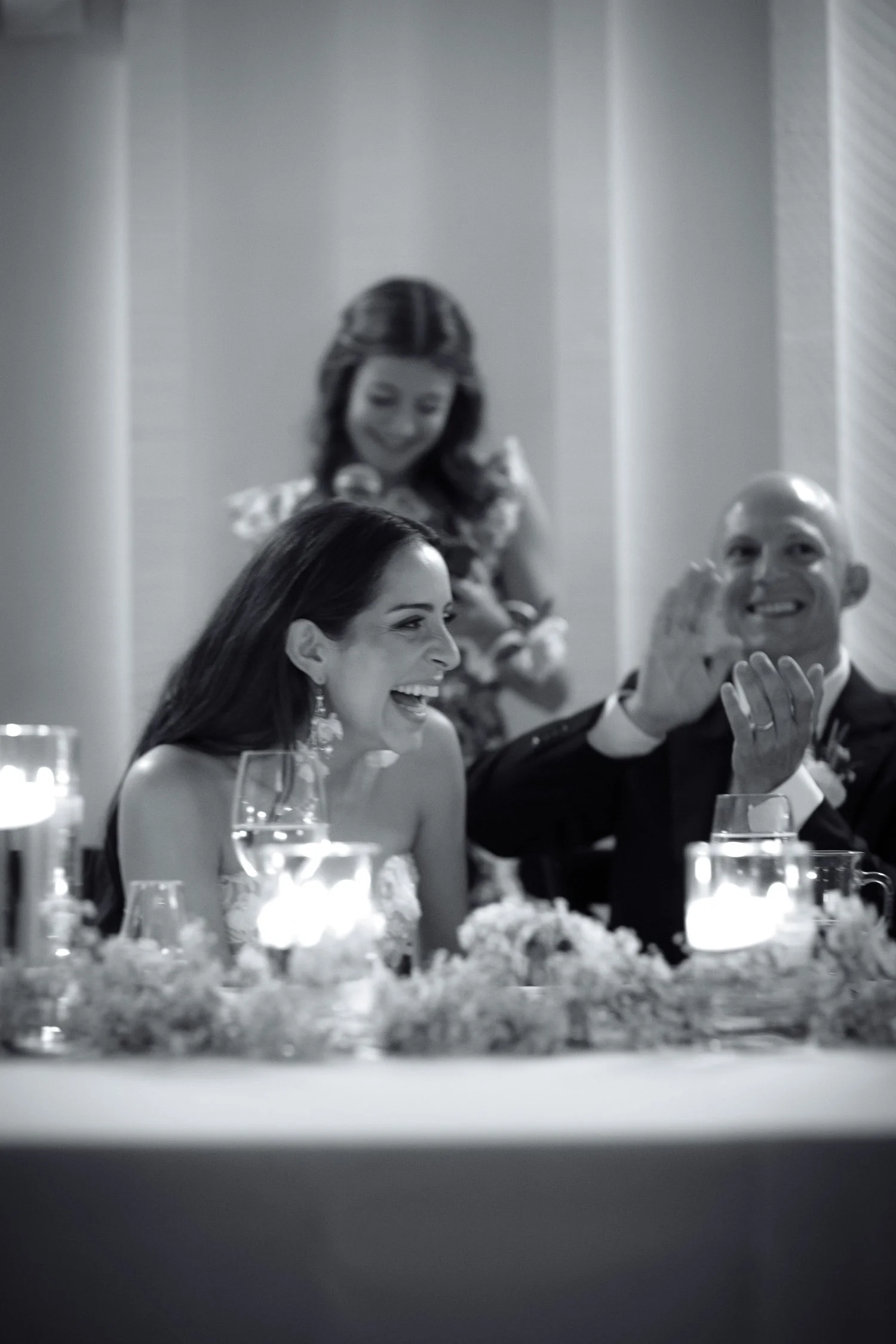 Bride laughing during a heartfelt wedding reception speech at candlelit head table