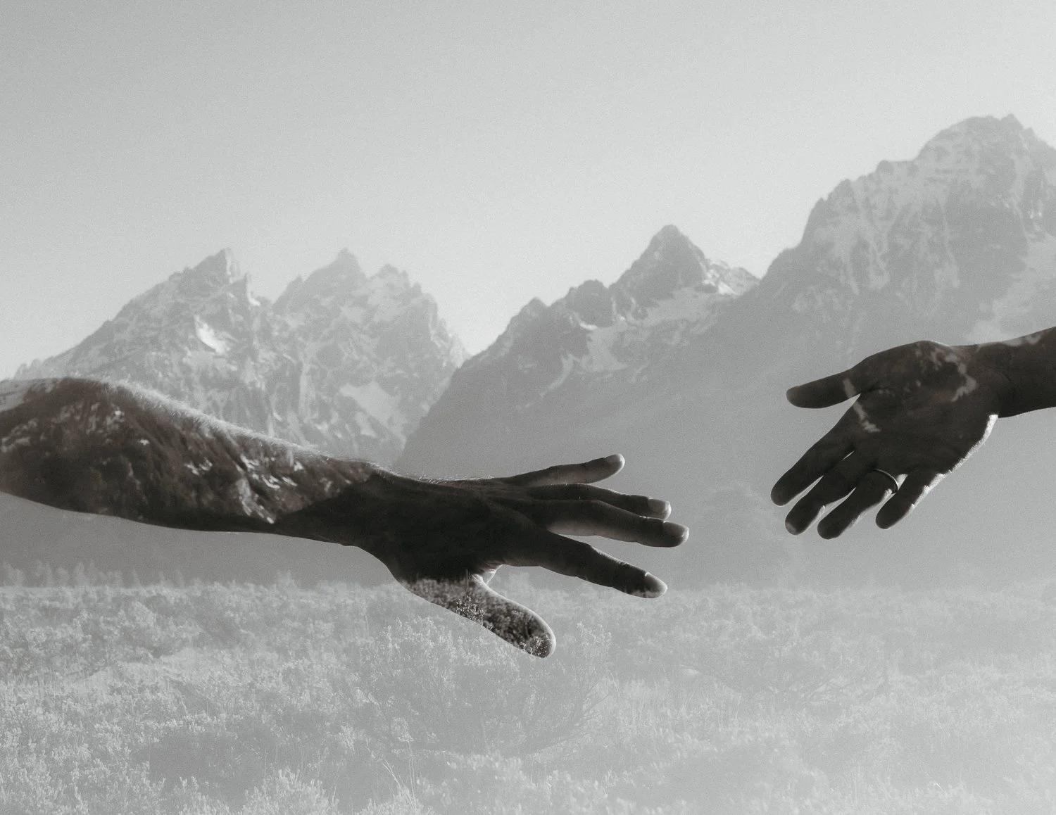 Artistic engagement photo of hands reaching with the Teton Range in the background