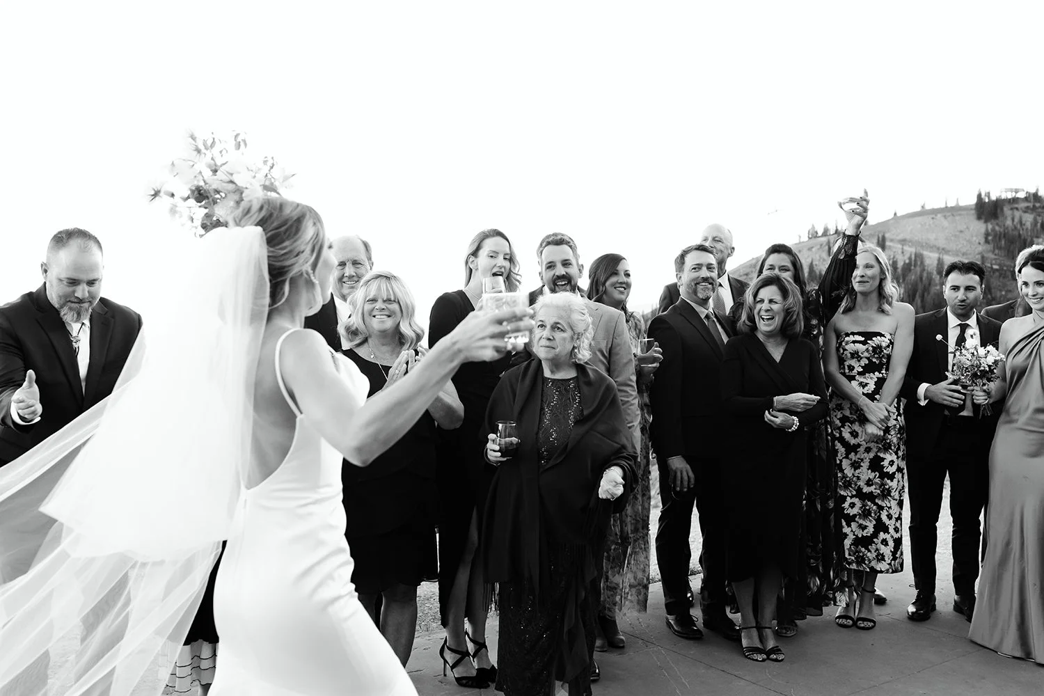 Family and guests raising glasses and reacting during an outdoor wedding celebration.
