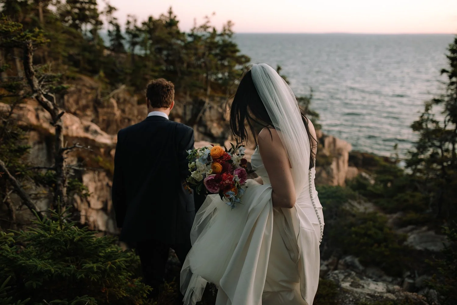 Bride and groom walking together through coastal trees during an Acadia National Park elopement evening