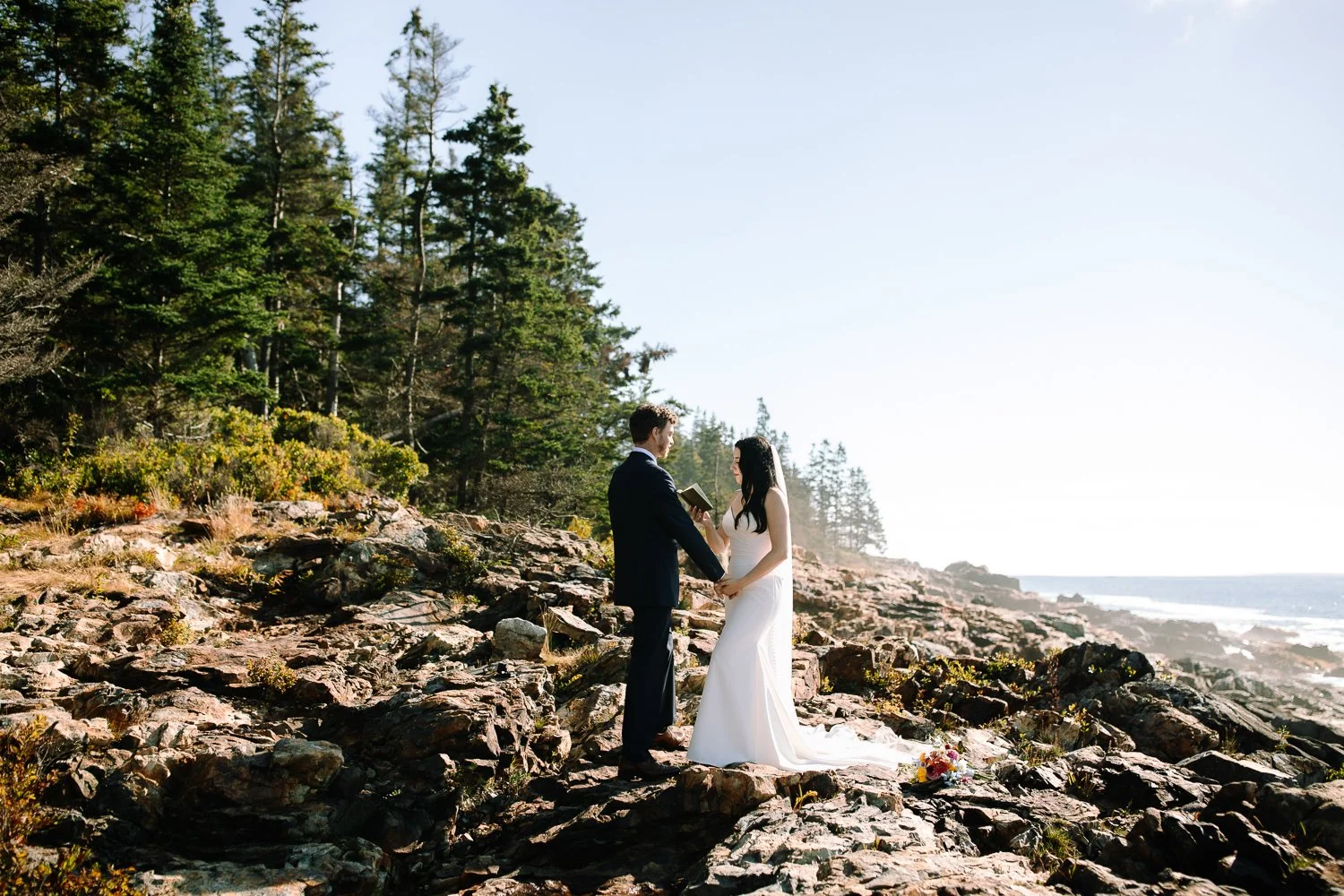 Wide view of bride and groom exchanging vows on the rocky coastline during an Acadia National Park elopement ceremony