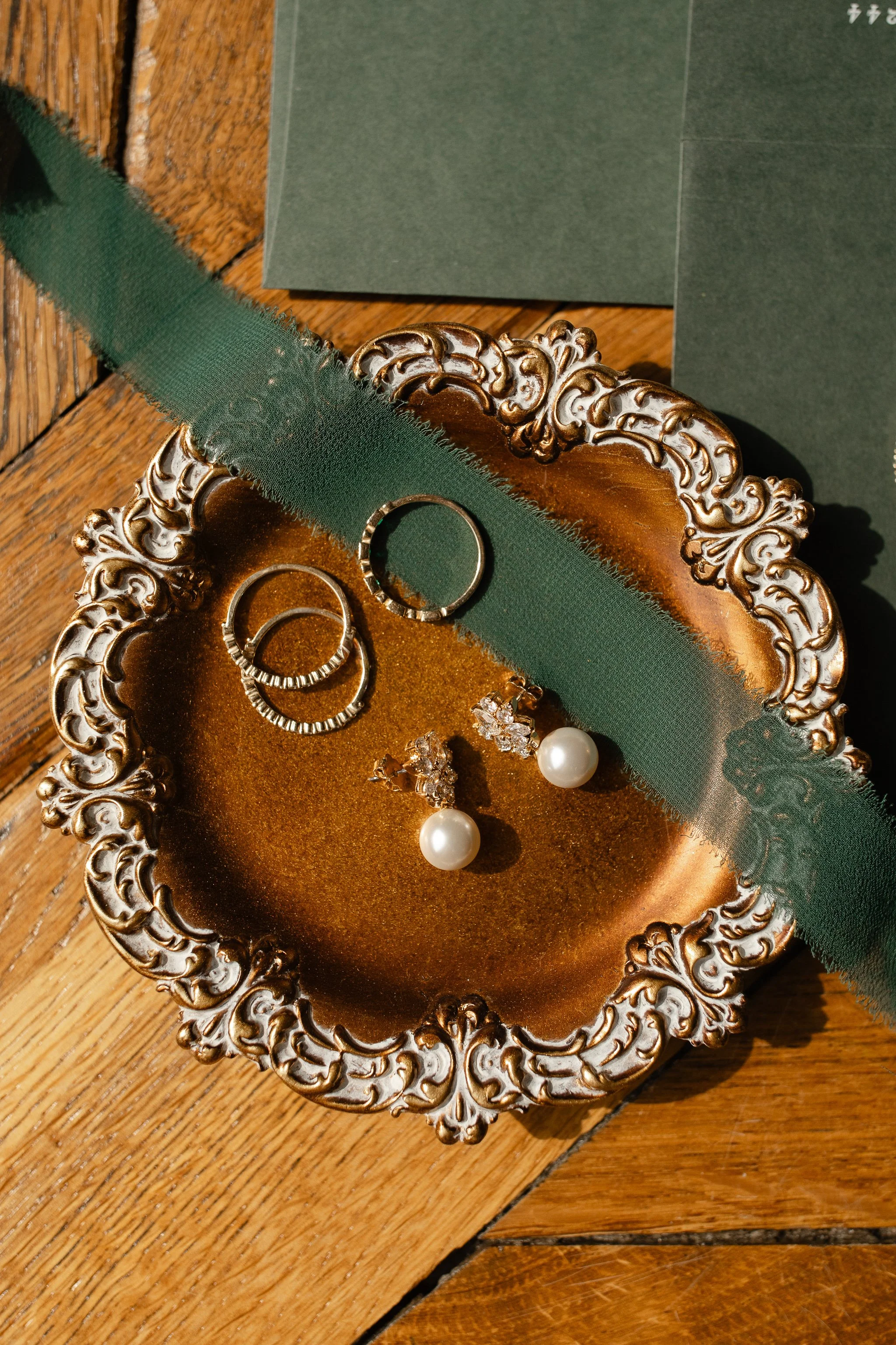 Bridal jewelry styled on vintage tray with green ribbon and paper goods
