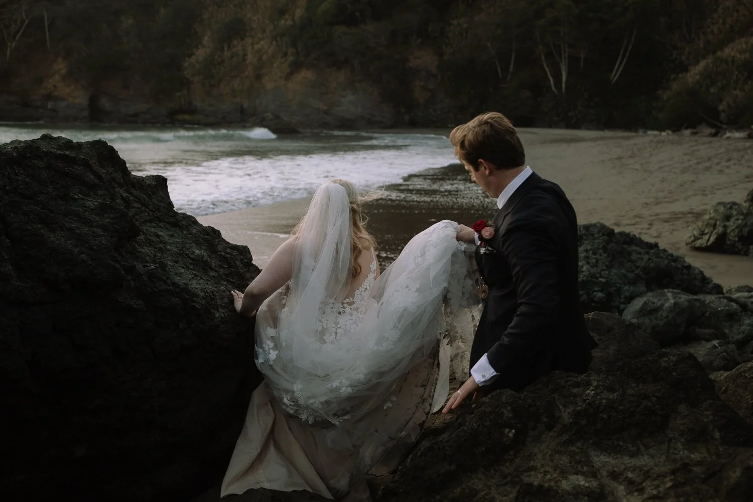 Bride and groom sitting together on coastal rocks overlooking the ocean