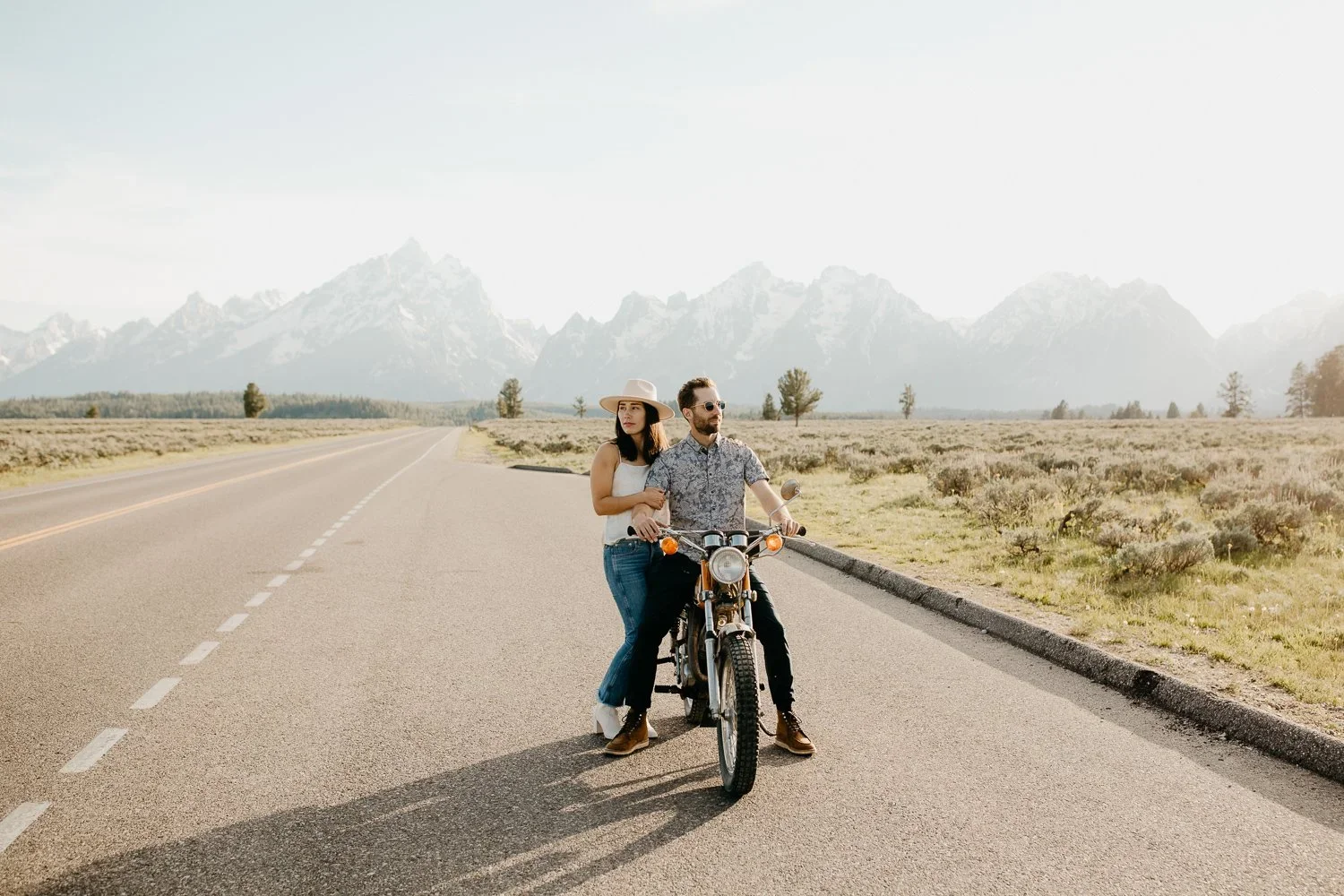 Engaged couple sitting on a motorcycle along a road in Grand Teton National Park