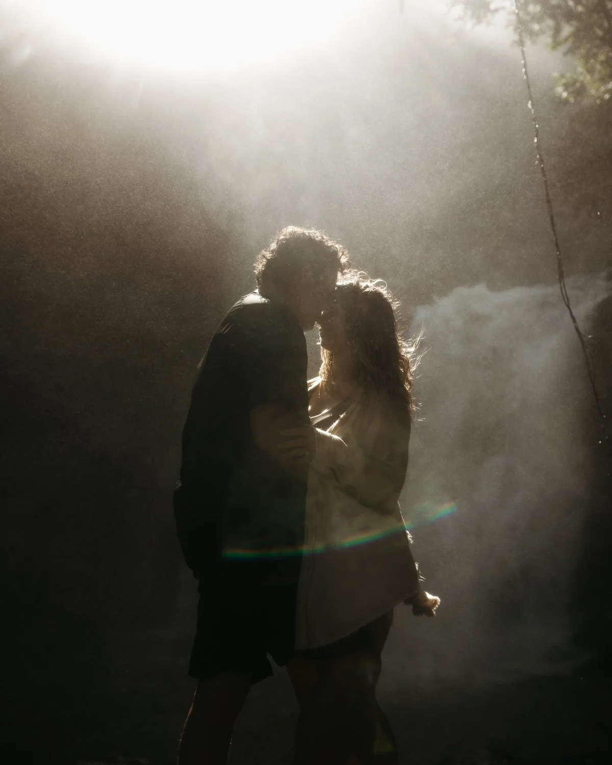 Couple embracing in soft backlight near a waterfall during an intimate elopement-style moment