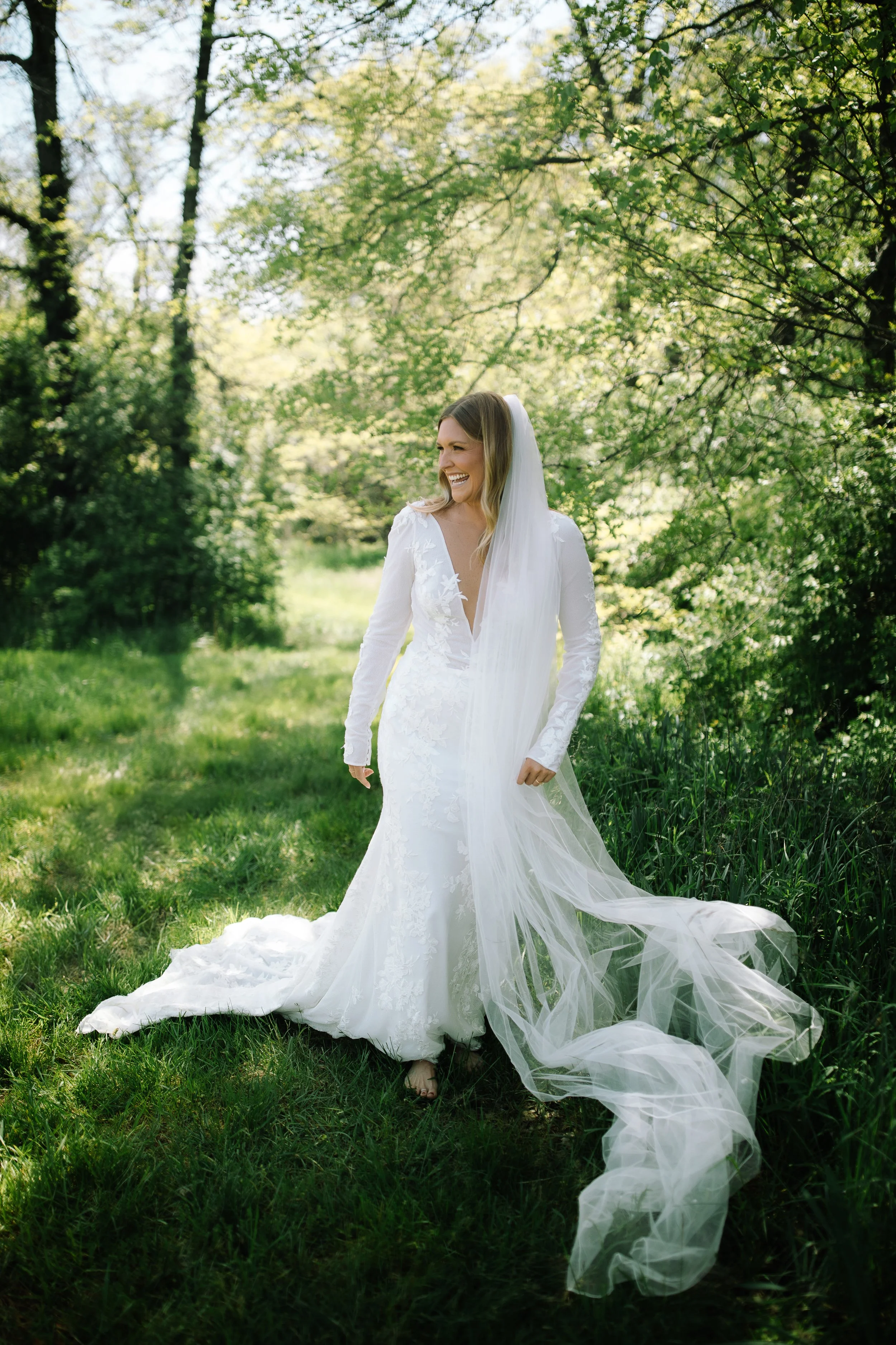 Bride standing barefoot in tall green grass with her veil flowing during a spring wedding at Jorgensen Farm The Gardens in Columbus, Ohio.