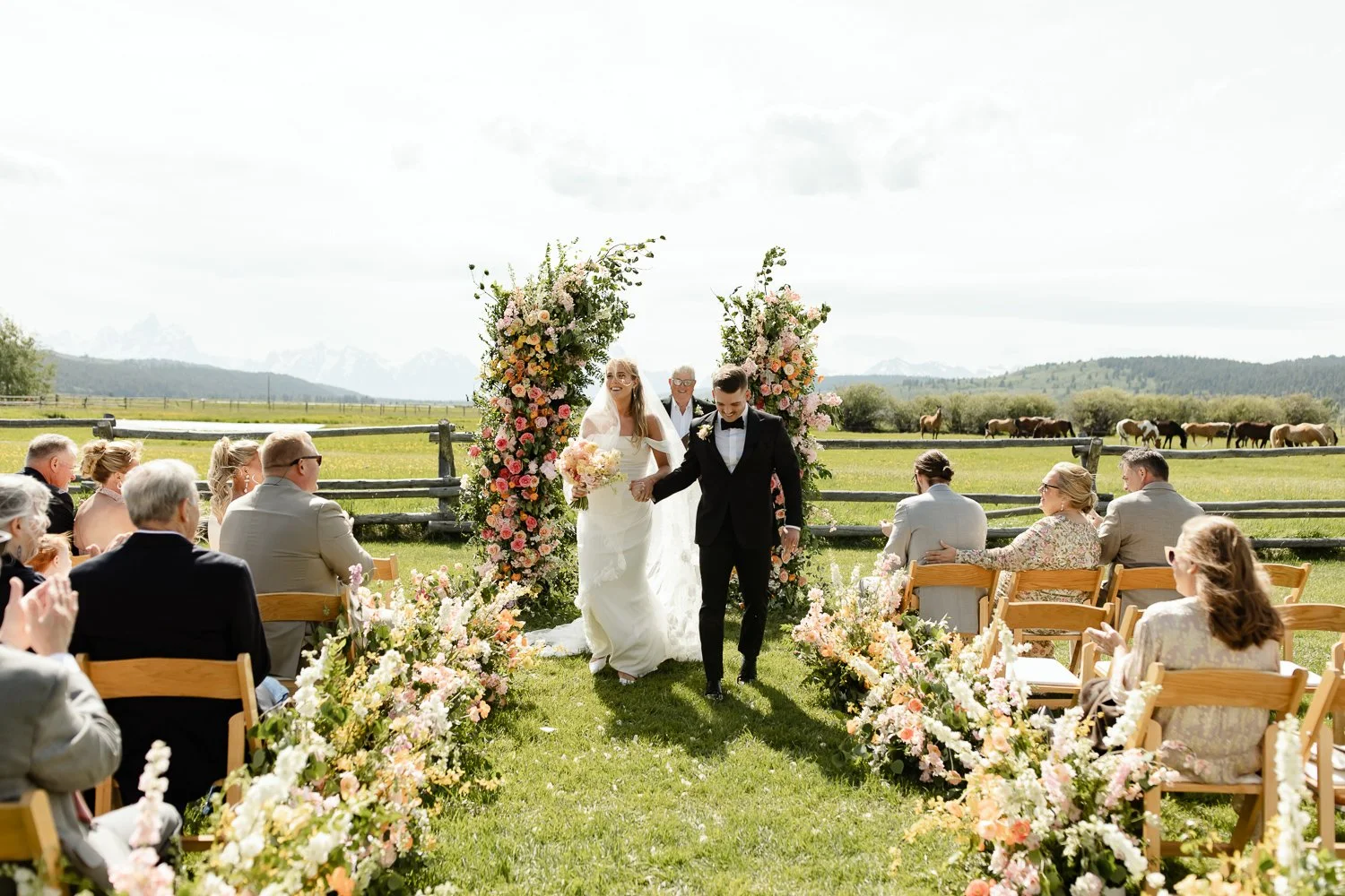 Wide view of outdoor wedding ceremony with floral arch, guests seated, and mountain landscape in Jackson Hole