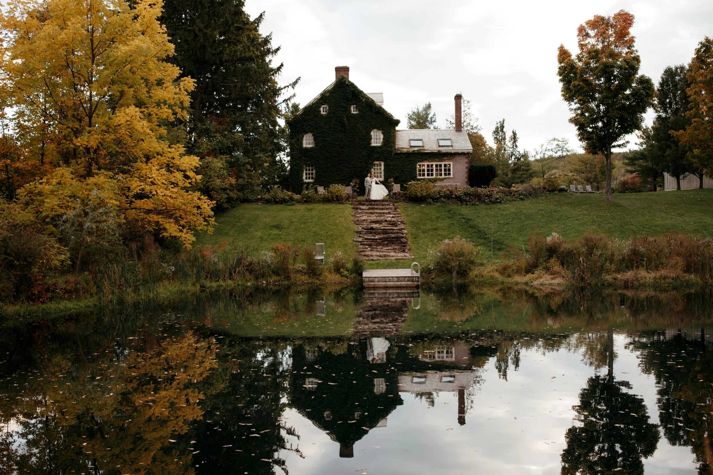Bride and groom standing by the pond at Windrift Hall during a fall Catskills wedding