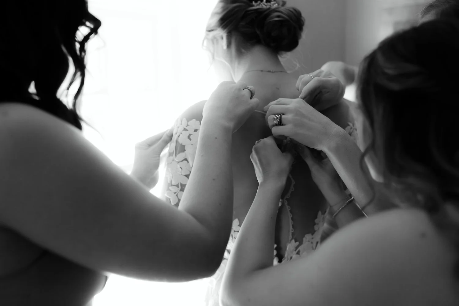 Bridesmaids fastening the back of the bride’s dress in a historic room at Windrift Hall in the Hudson Valley