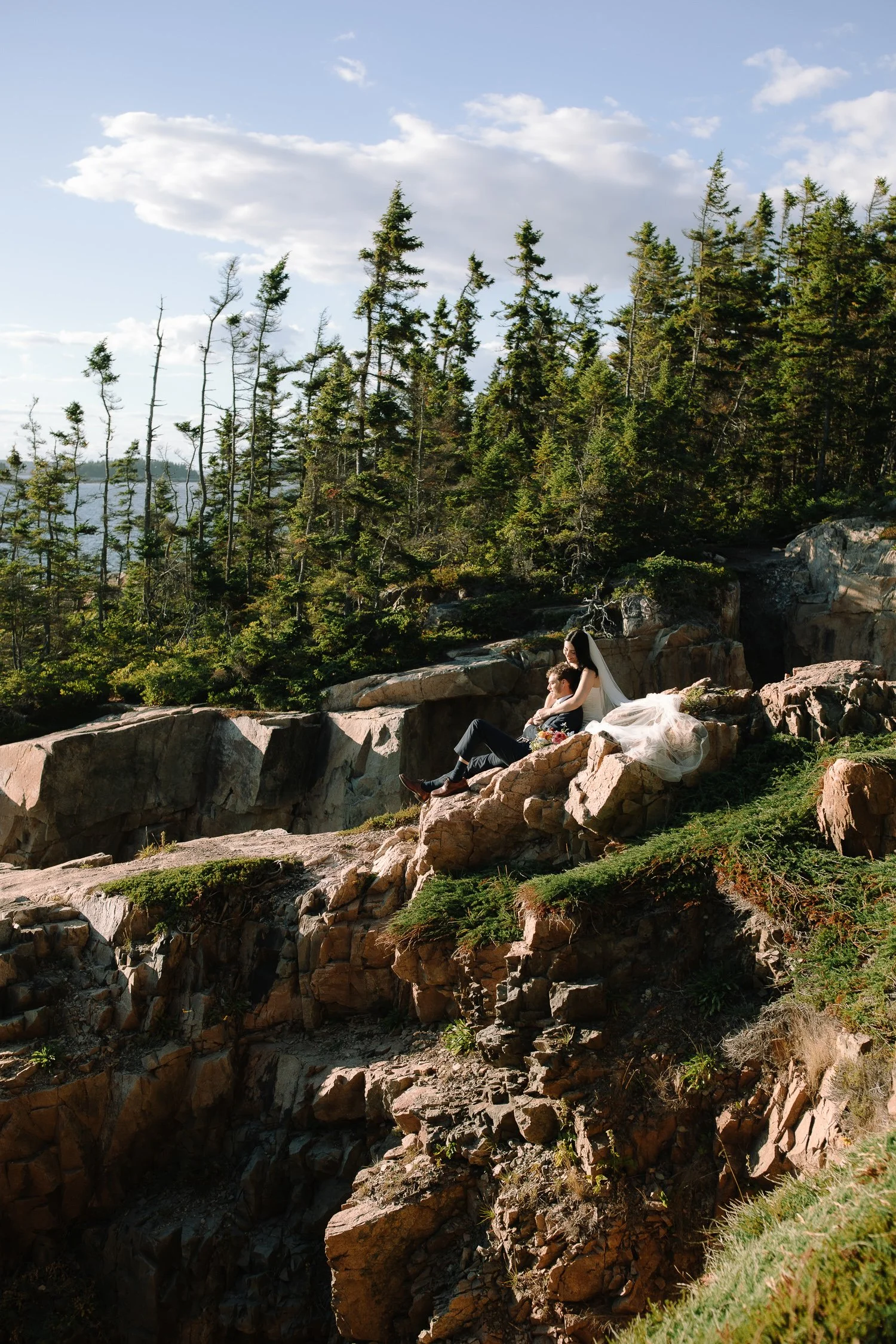 Bride and groom resting together on remote coastal cliffs during a sunset elopement in Acadia National Park