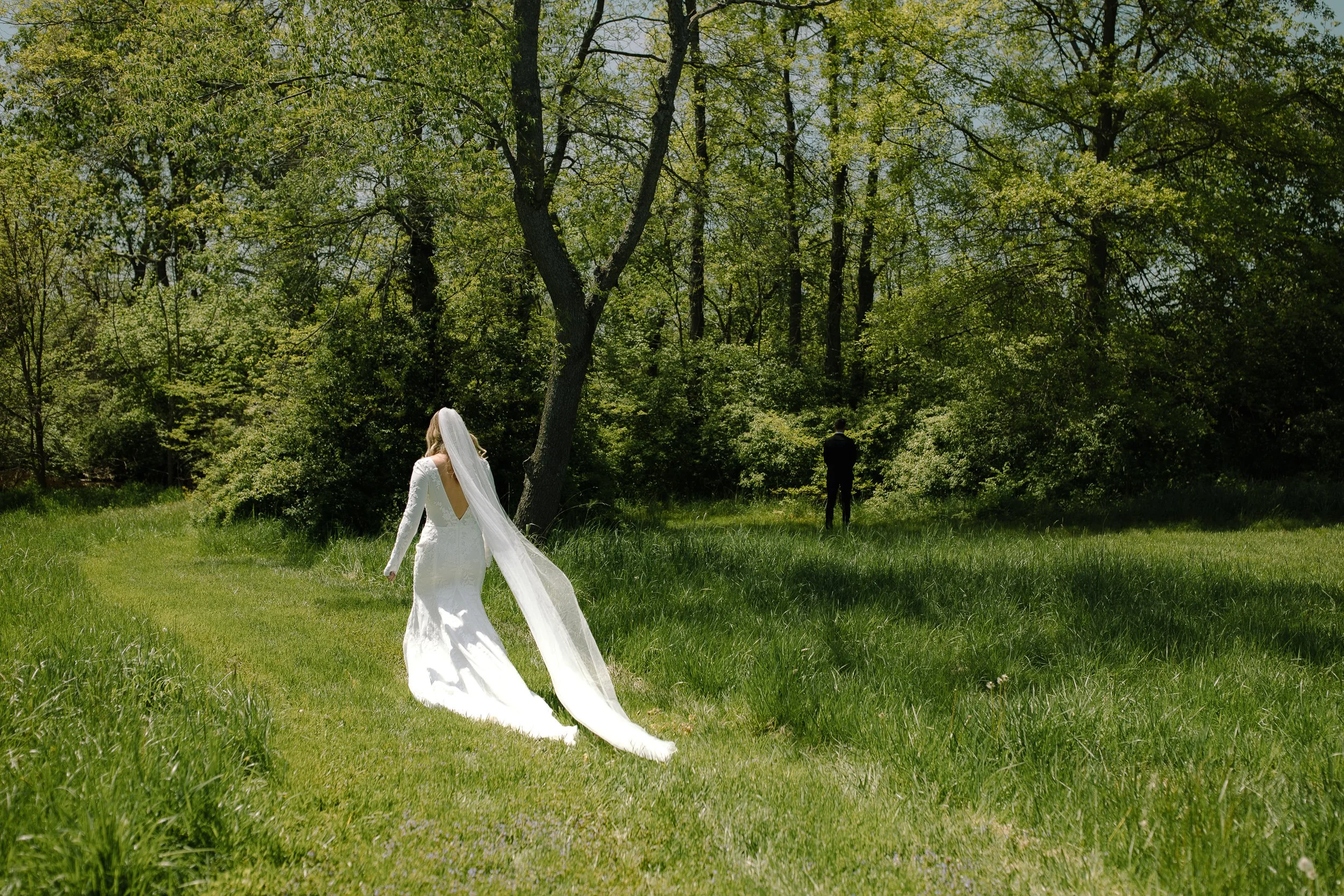 Bride walking through tall green grass toward her groom for a private first look at Jorgensen Farm The Gardens in Columbus, Ohio.