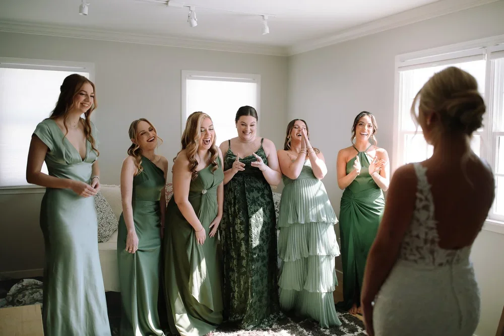 Bridesmaids reacting emotionally during a first look with the bride in a softly lit getting ready space.