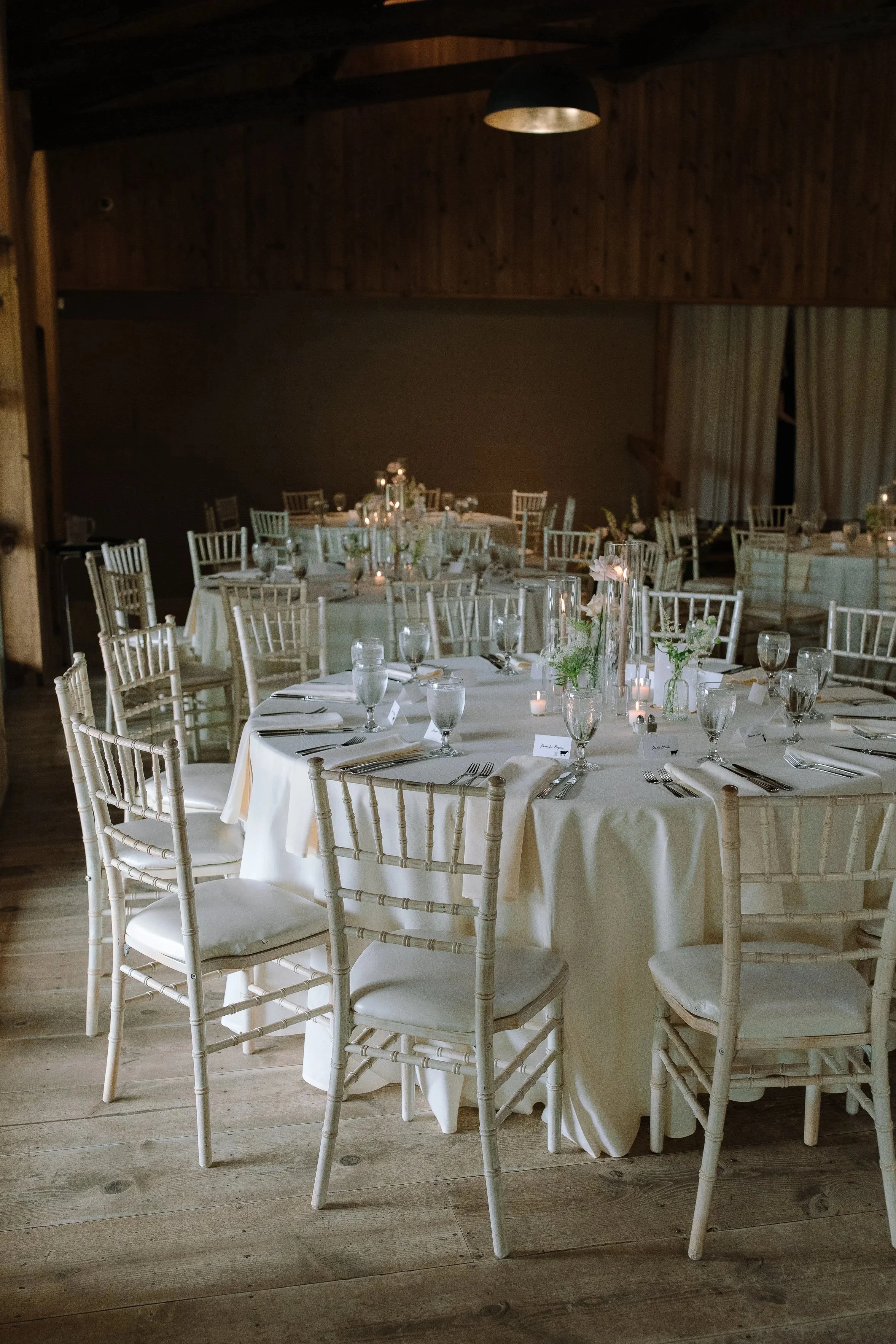 Round reception tables with candles and white chairs inside the historic barn at Jorgensen Farms in Columbus.
