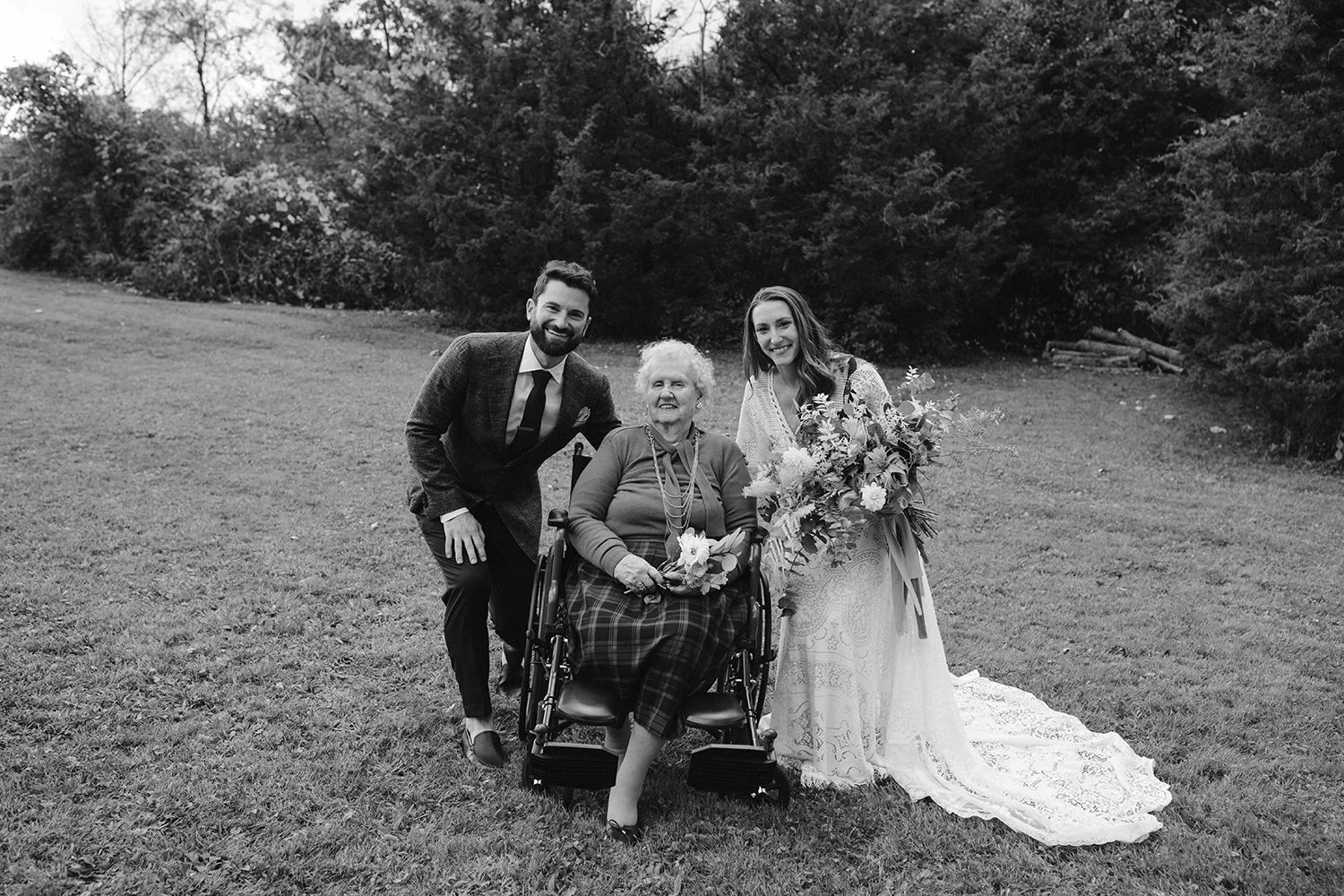 Bride and groom posing with grandmother in wheelchair during wedding day, meaningful family photo