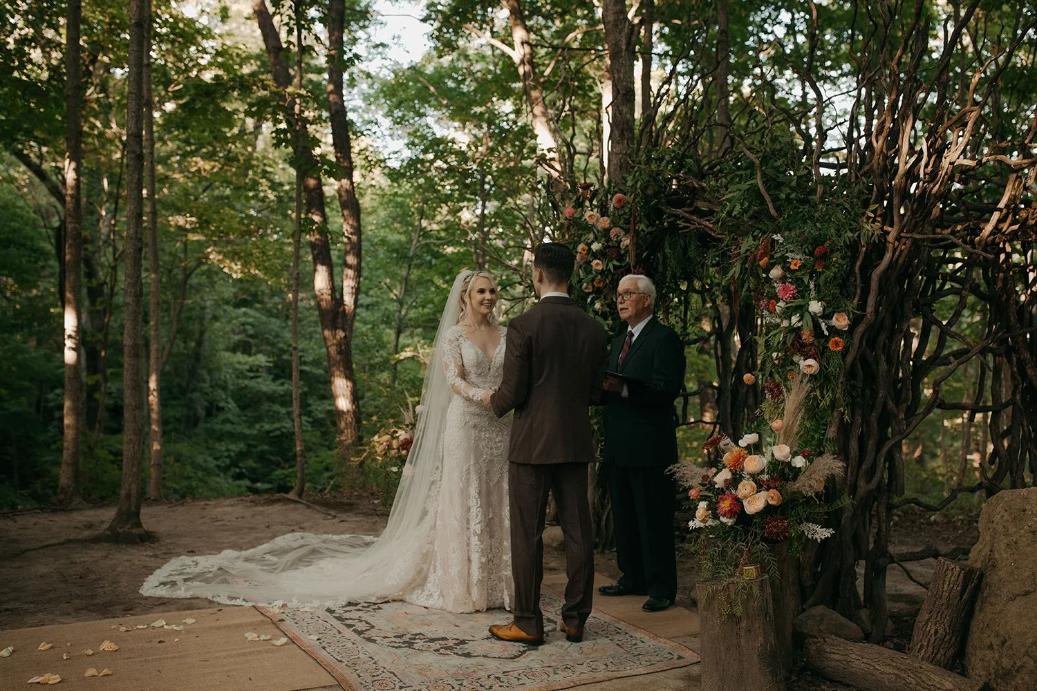 Outdoor woodland wedding ceremony at Canyon Run Ranch near Dayton, Ohio, with a couple exchanging vows beneath a natural branch arch in the forest.