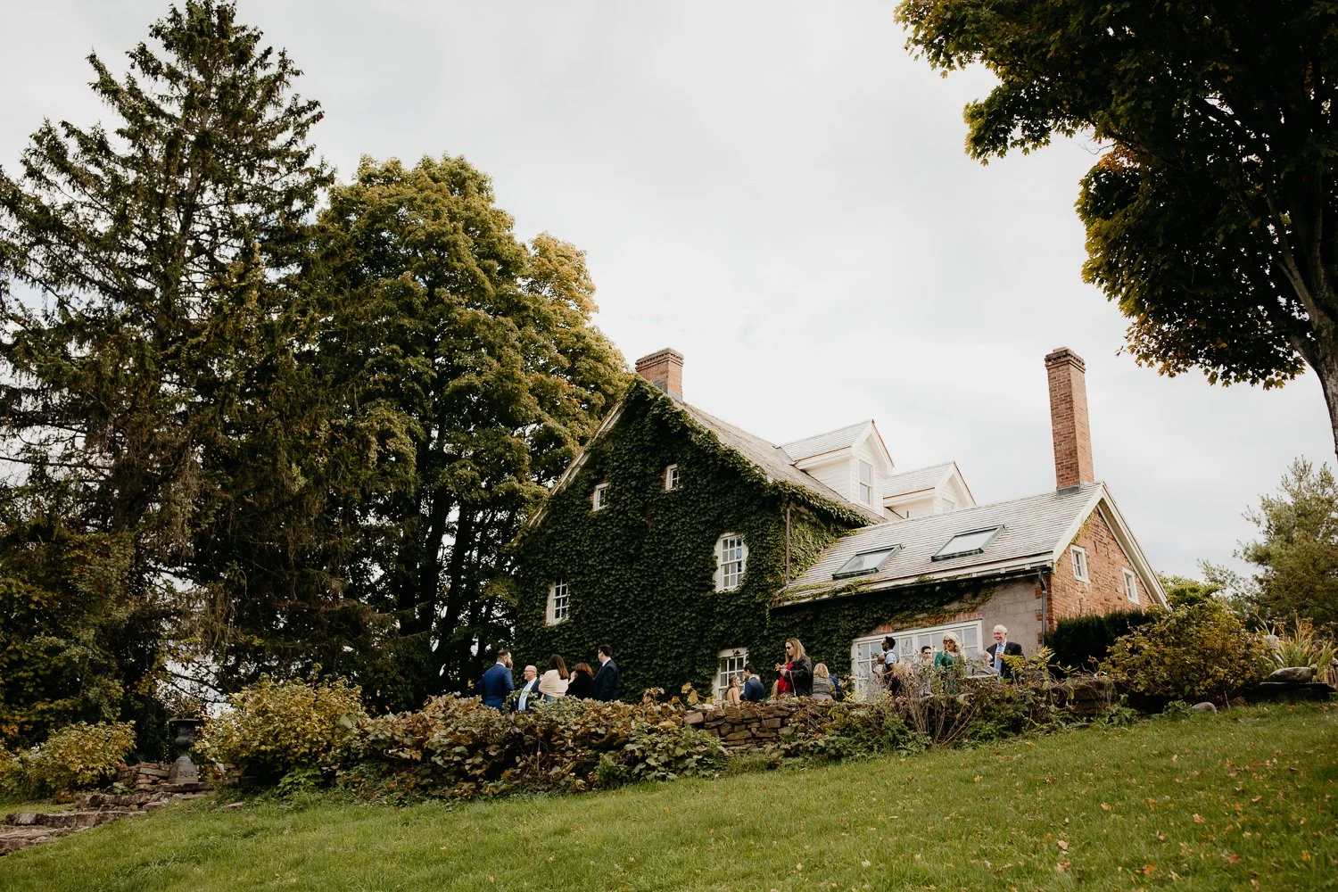 Guests enjoying cocktail hour outside the ivy covered Windrift Hall estate in the Hudson Valley