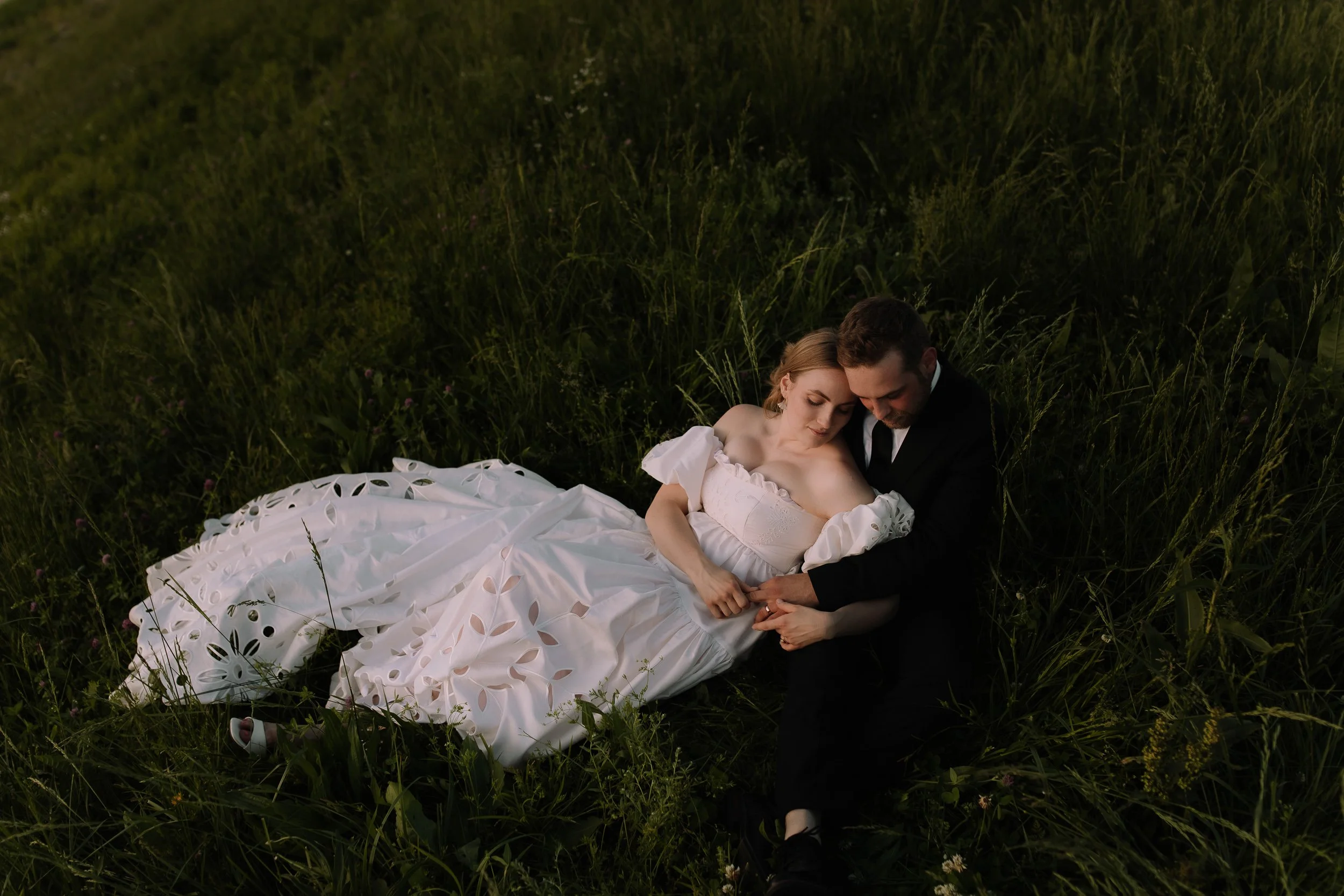 Bride and groom lying together in tall grass during golden hour near Dayton, Ohio