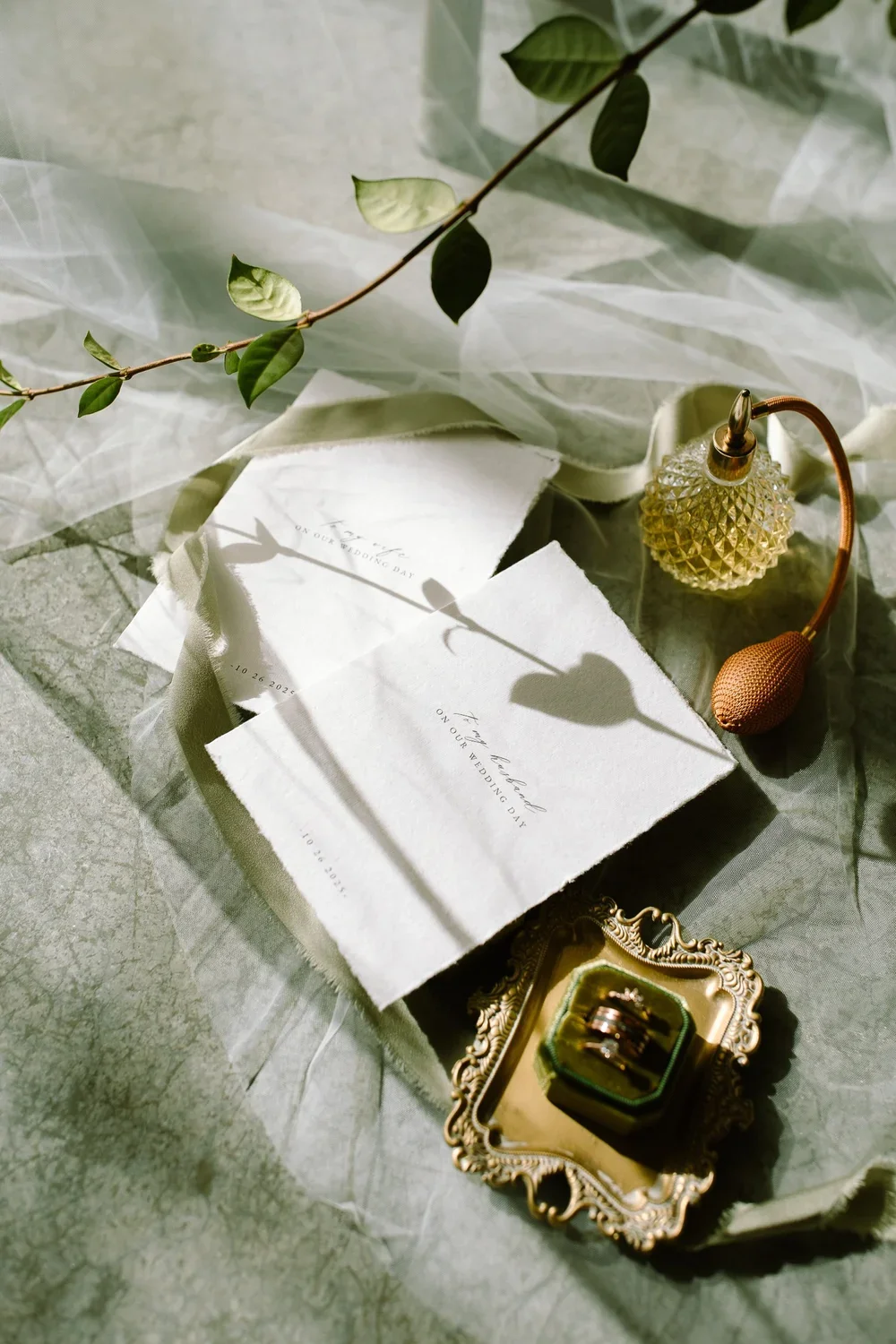 Garden-inspired wedding invitation suite styled with green silk ribbon, gold tray, and heirloom ring box.