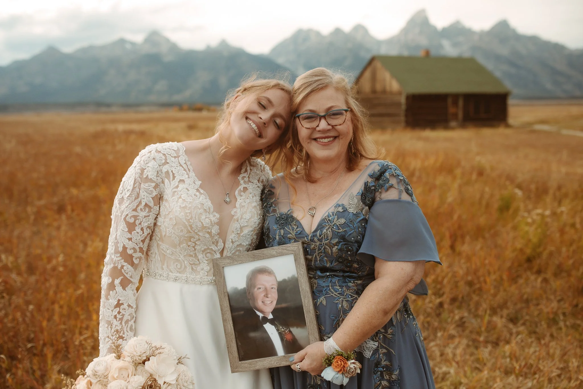 Emotional portrait of bride and mother honoring a missing family member with framed photo in the Tetons