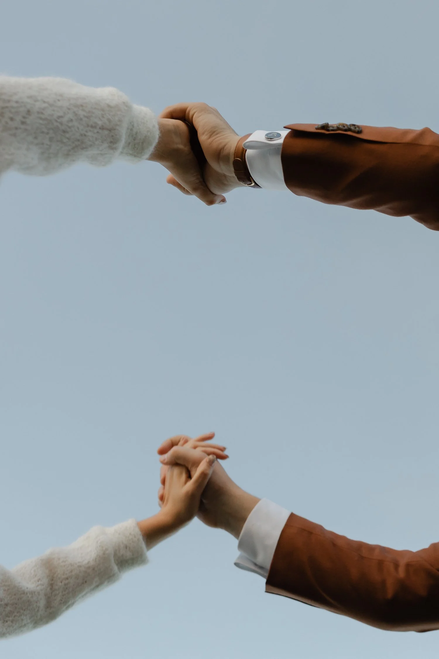 A close-up shot of the bride and groom's hands holding each other against a clear sky backdrop, symbolizing unity during their joy-filled October wedding.