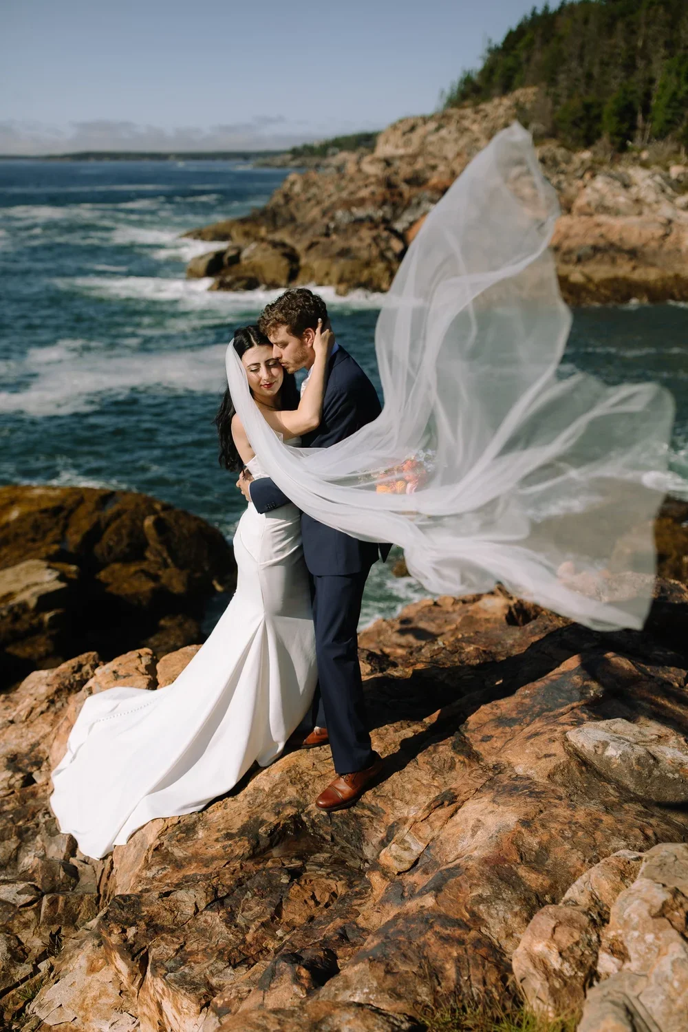 Eloping couple embracing on windy coastal cliffs in Acadia National Park, Maine