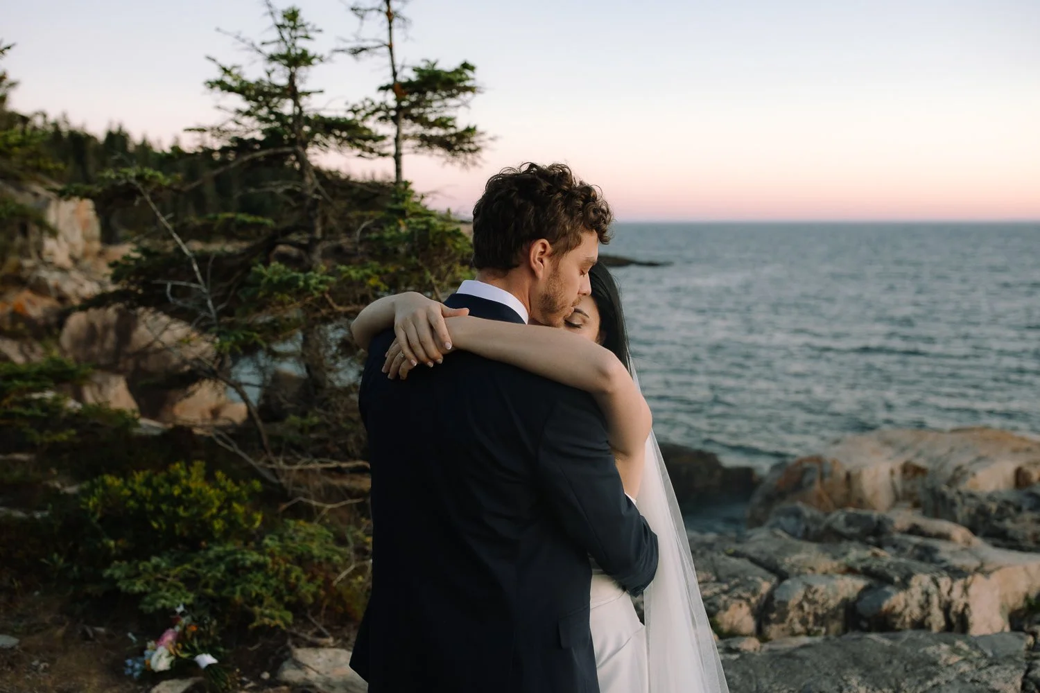Bride and groom holding each other quietly along the rocky coastline during an Acadia National Park elopement