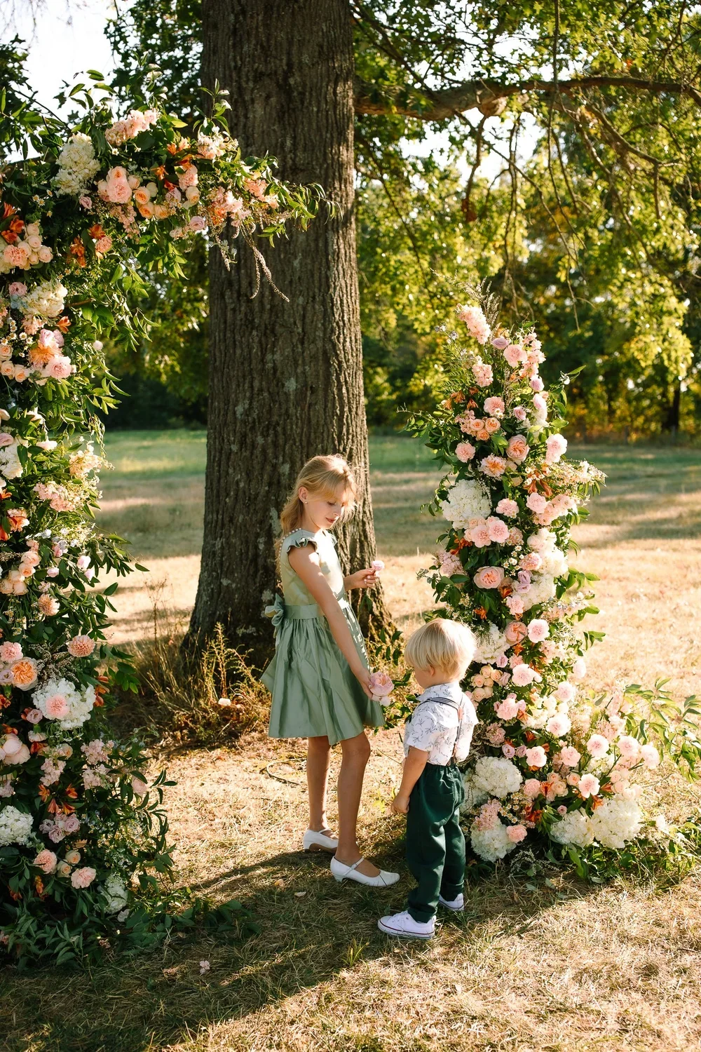 Two young children standing beneath a floral ceremony arch at Oak Grove at Jorgensen Farms near Columbus, Ohio