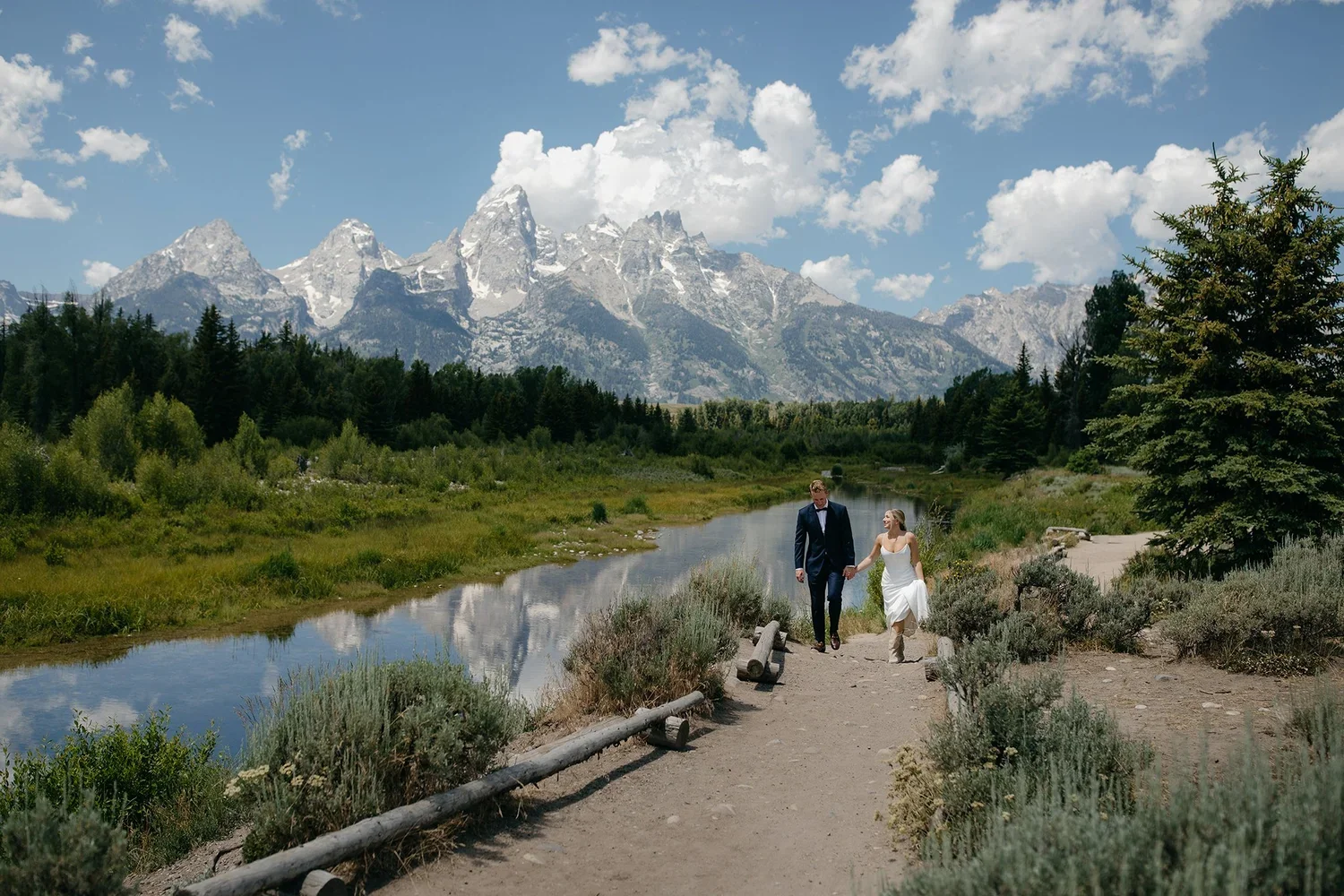 Couple walking hand in hand along a path with the Grand Teton mountain range in the background.