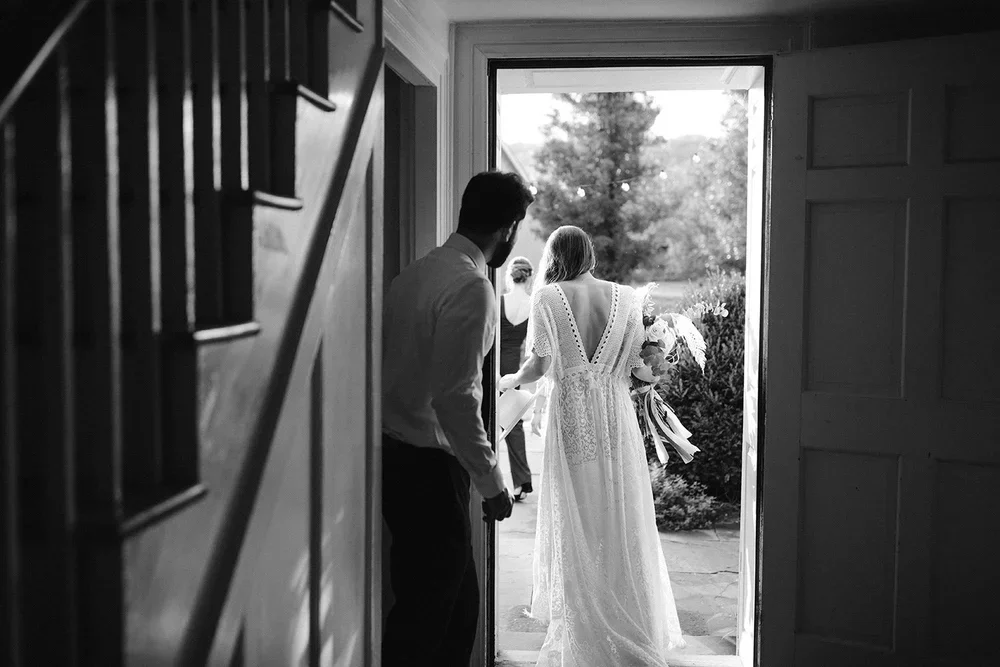 Bride and groom walking through doorway into ceremony space captured in candid black and white