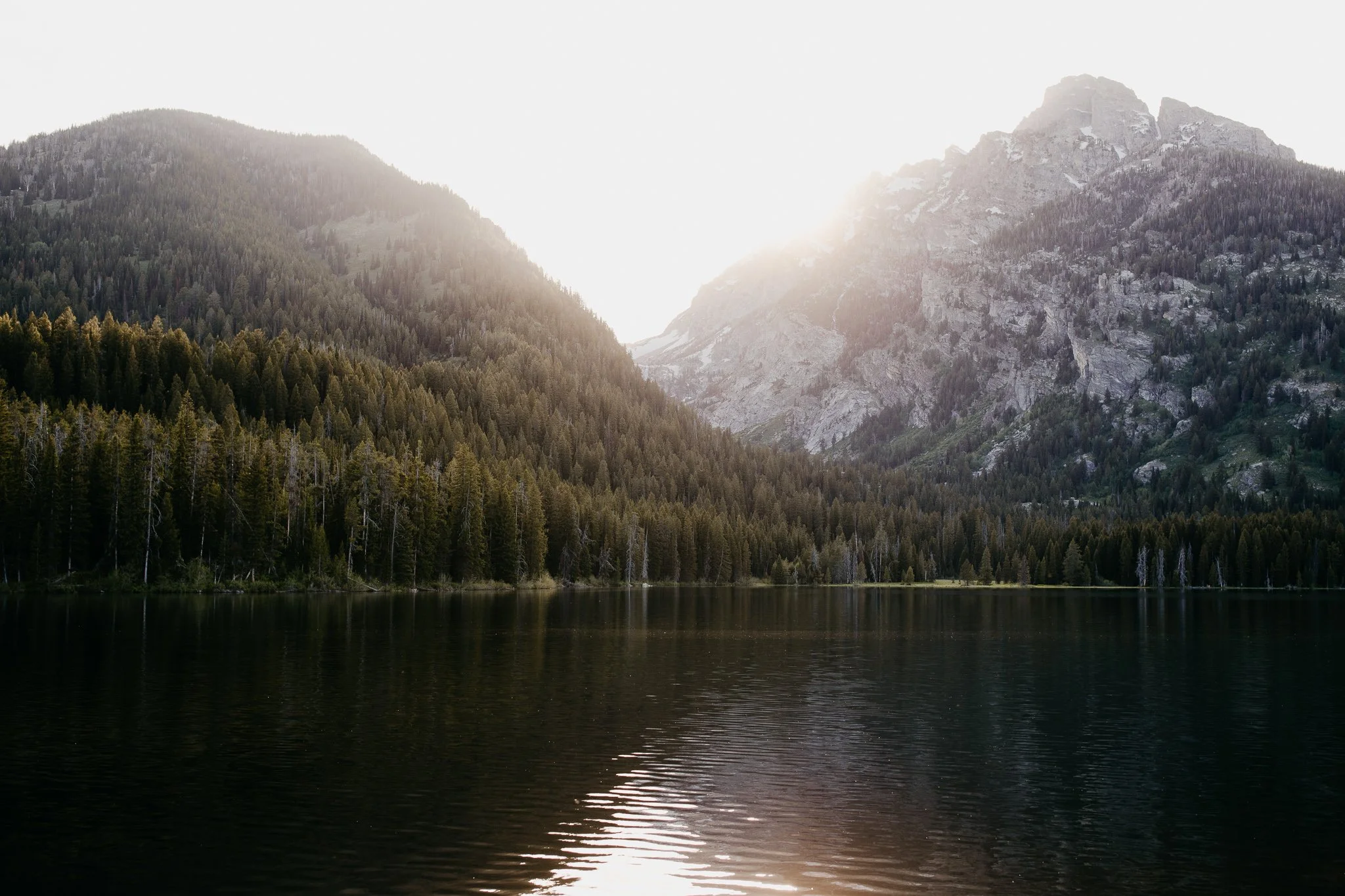 Sunlight reflecting across an alpine lake surrounded by mountains in Grand Teton National Park
