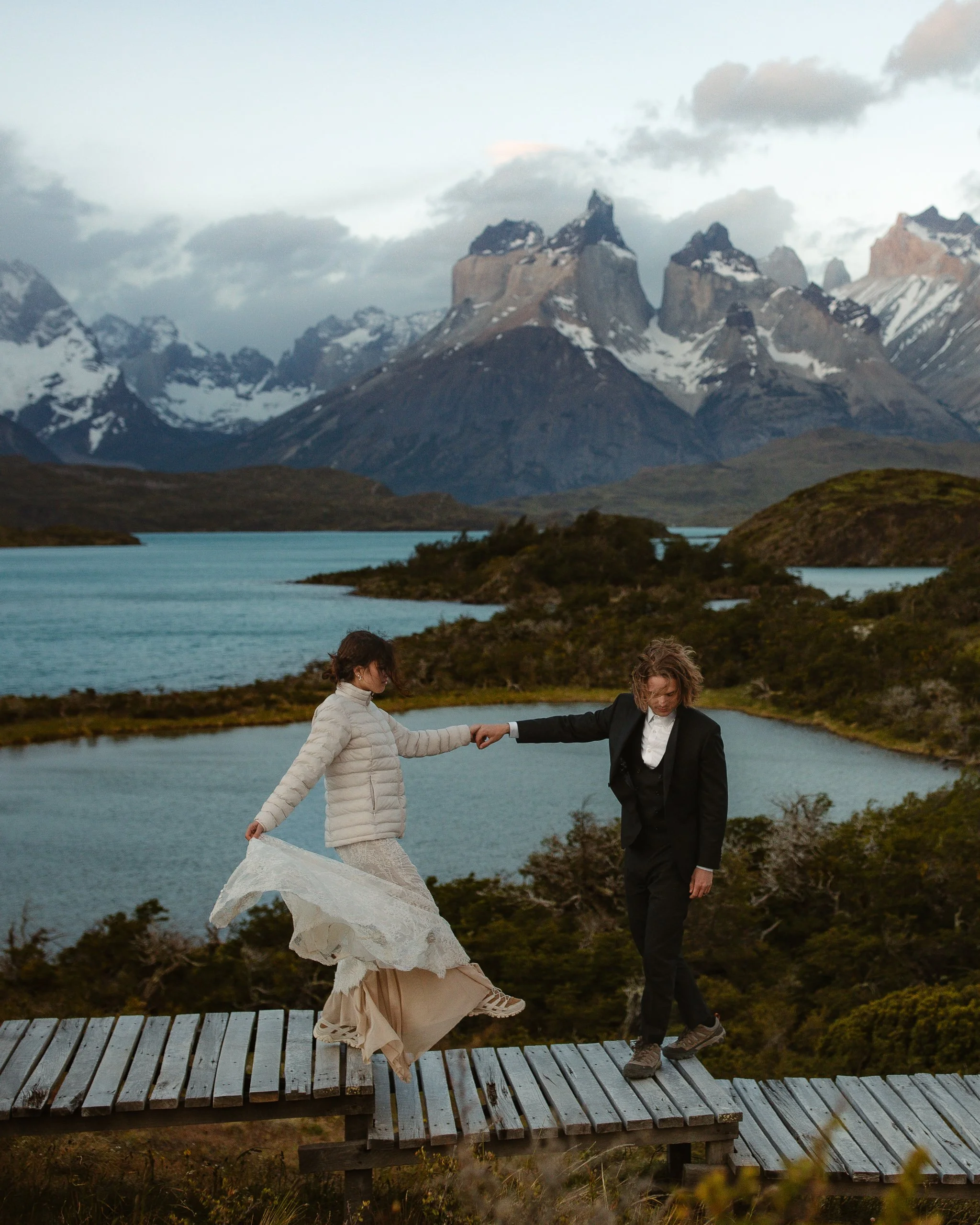 Couple walking hand in hand on a boardwalk overlooking the serene blue lakes and picturesque mountains of Torres del Paine in Patagonia