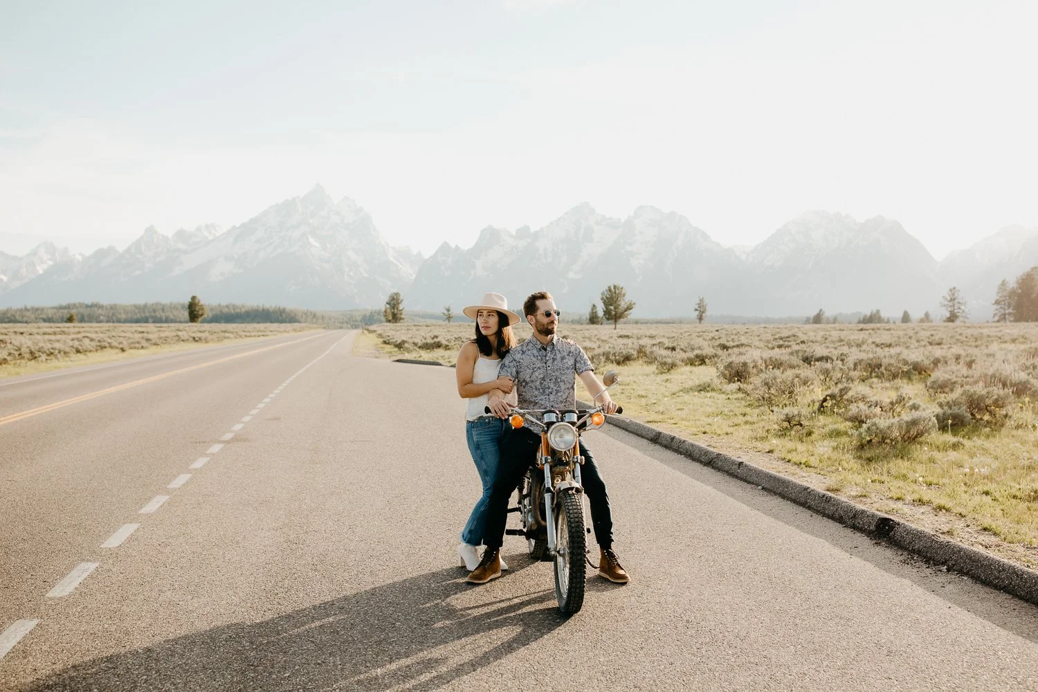 Couple standing with a vintage motorcycle on a quiet road in Grand Teton National Park